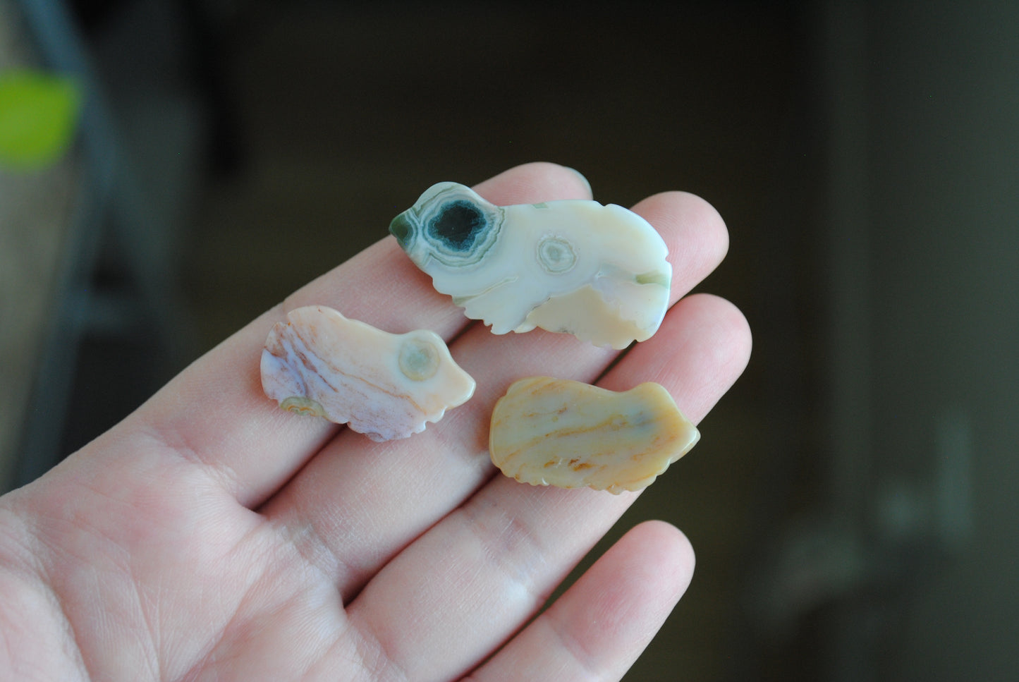 Three small stone frog carvings held in a hand against a blurred background