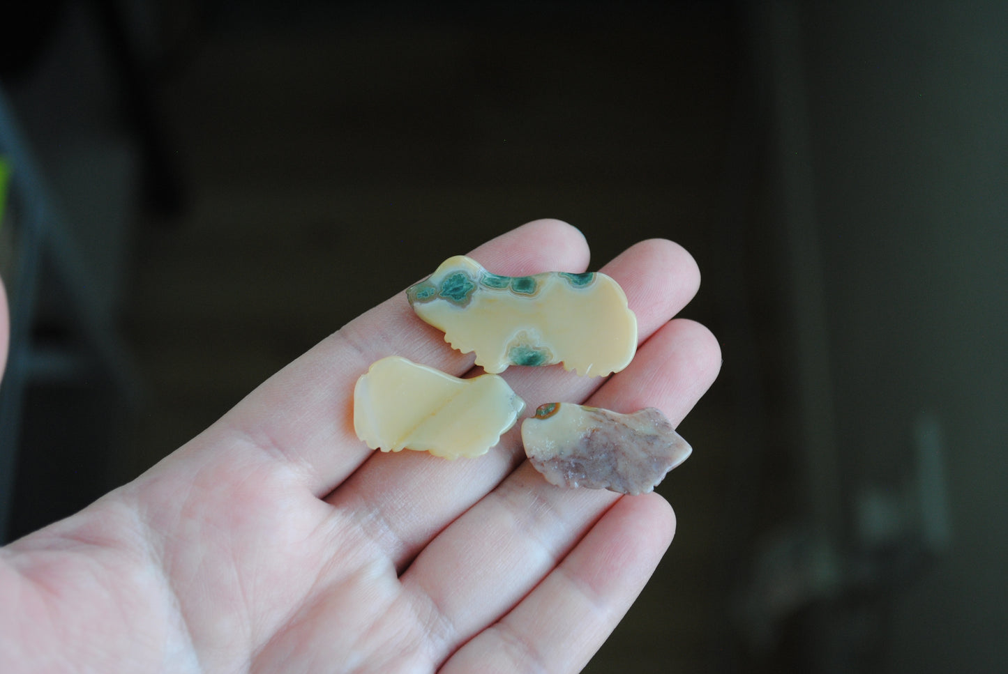 Three small stone frog carvings held in a hand against a blurred background