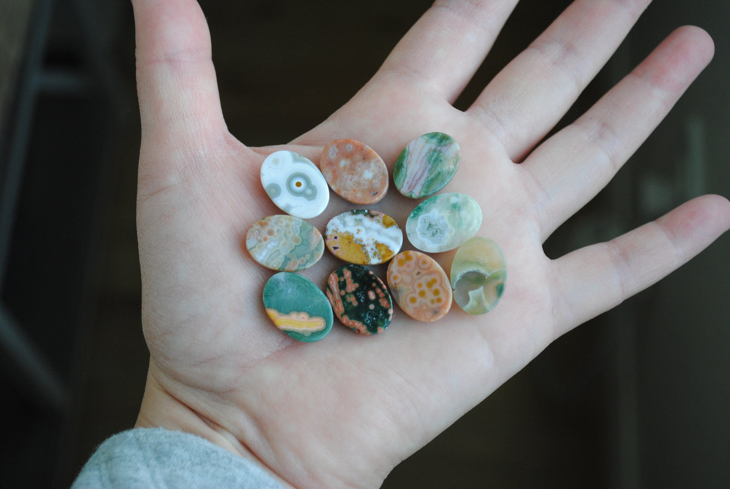 Hand holding a collection of small, multicolored stones against a dark background