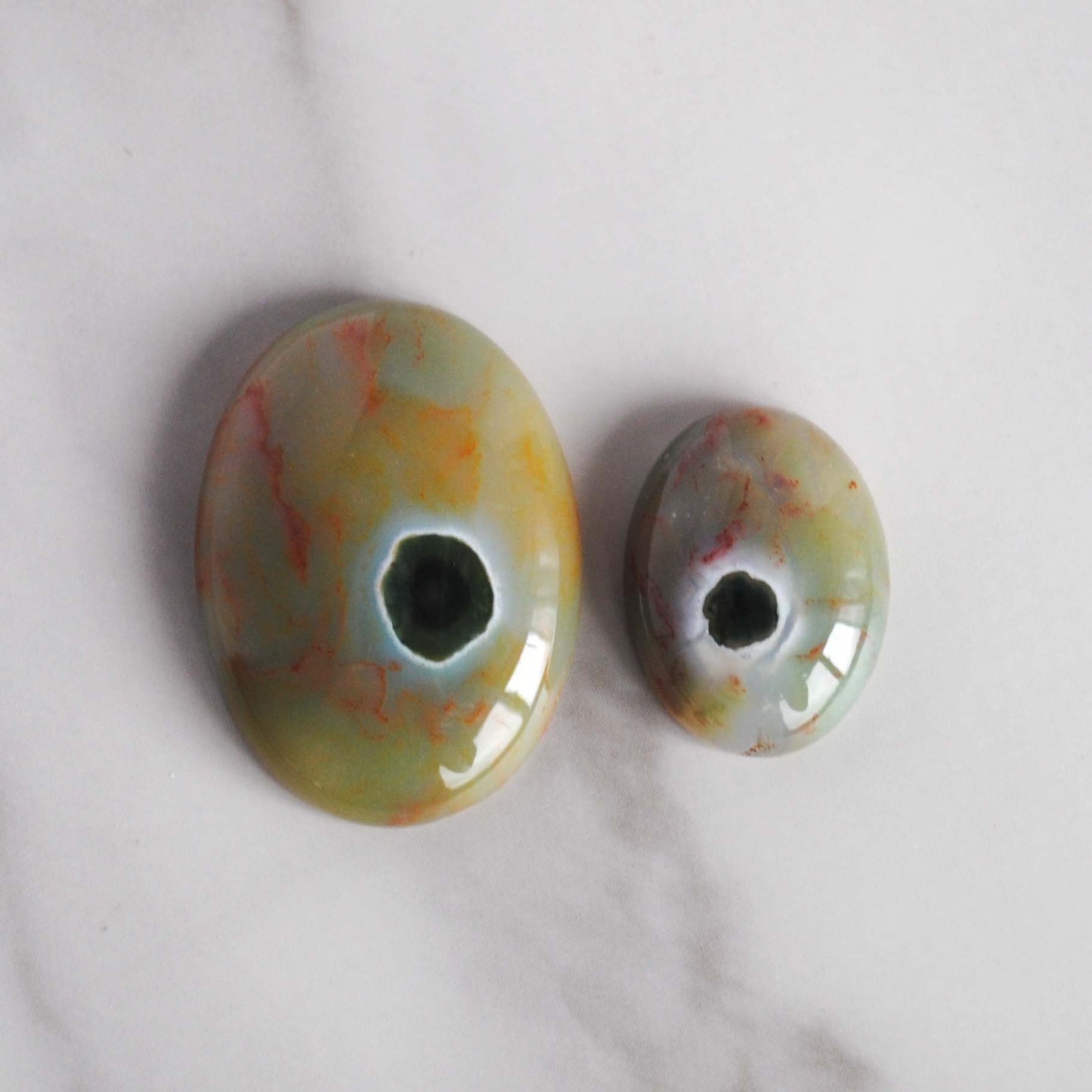 Two oval-shaped Ocean Jasper cabochons with a marbled green and brown appearance, placed on a white surface.