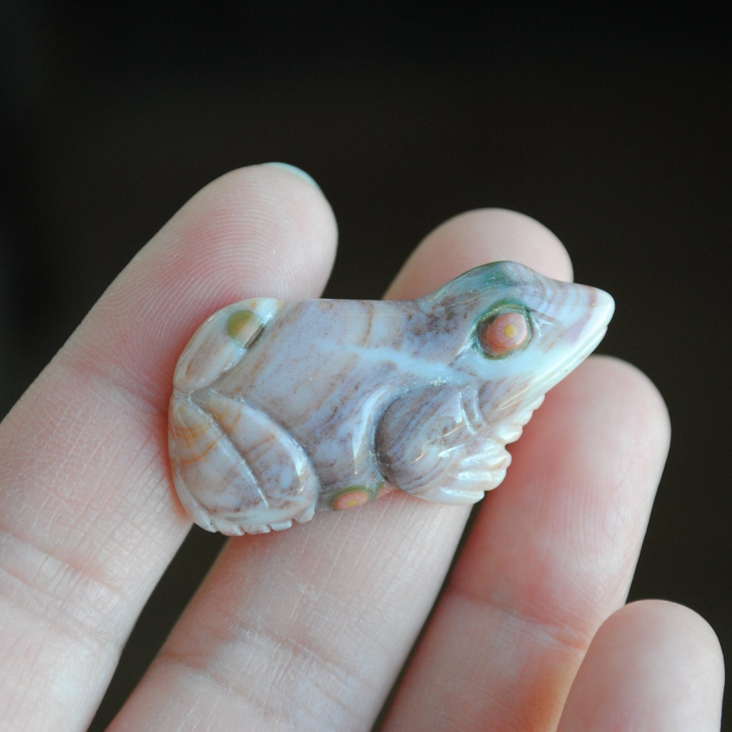 Carved stone frog held in a hand against a dark background