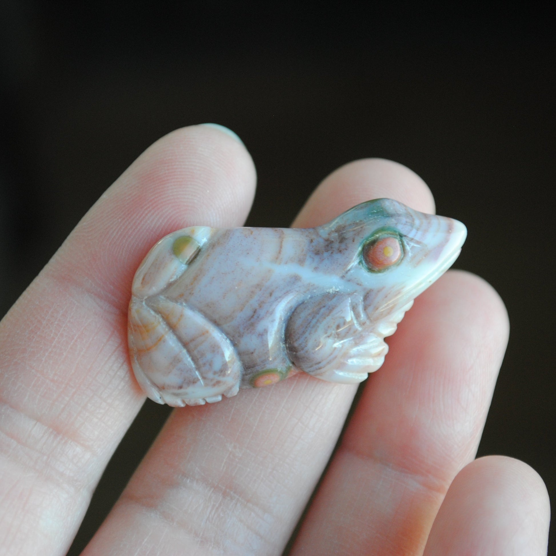Carved stone frog held in a hand against a dark background