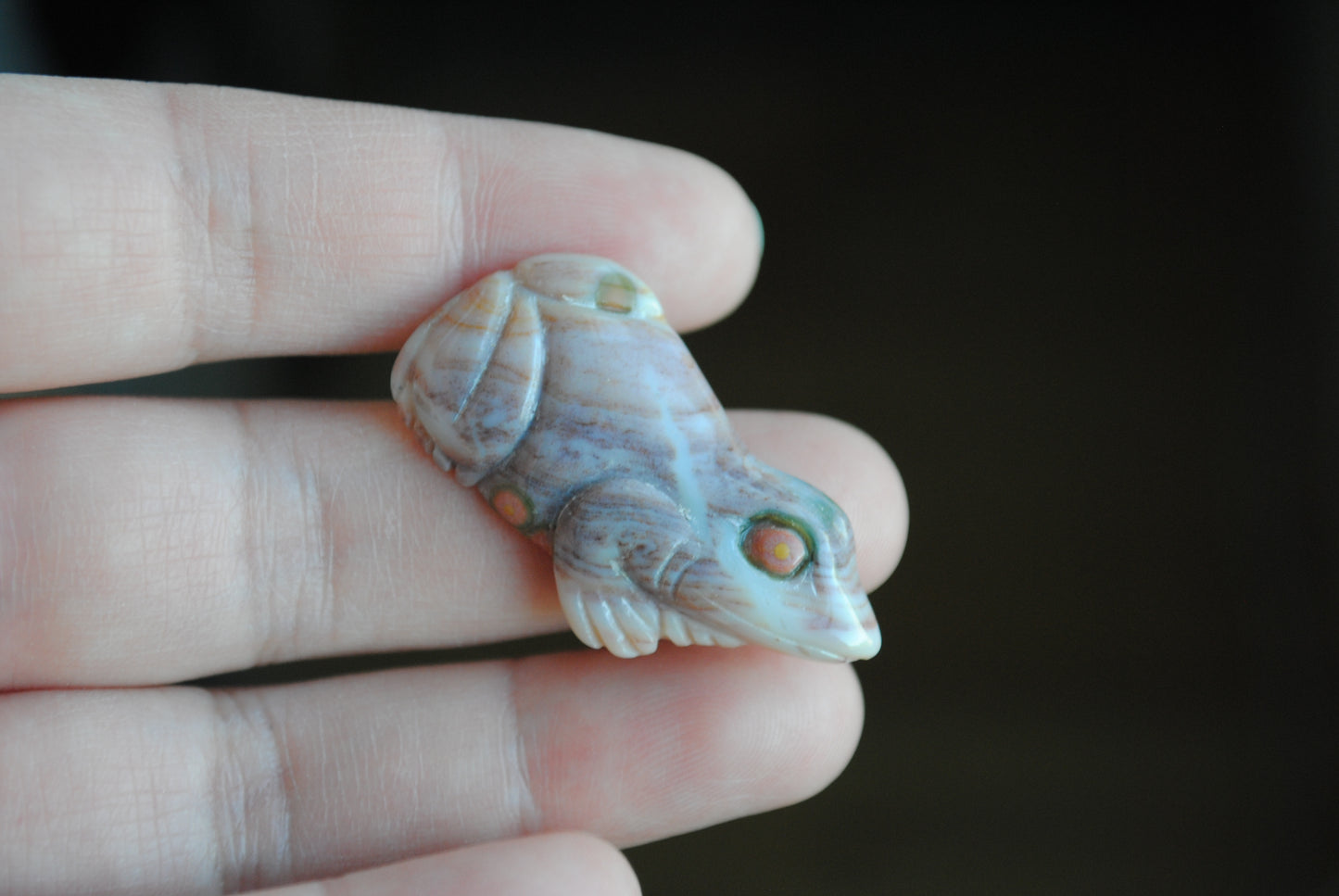 Carved stone frog held in a hand against a dark background