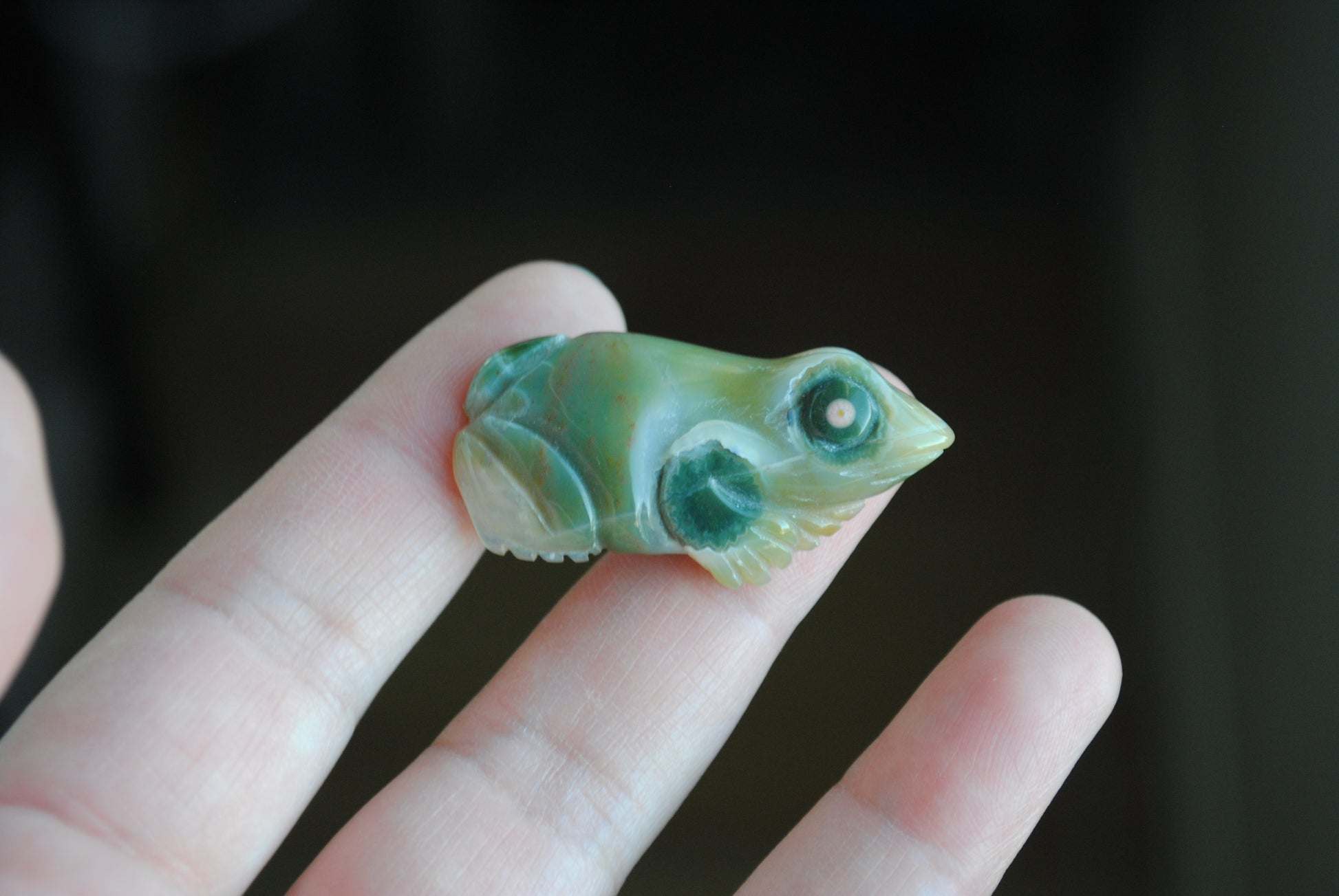 Carved stone frog held in a hand against a dark background