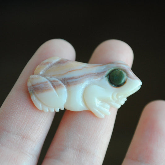 Small stone carving of a frog held in a hand against a dark background