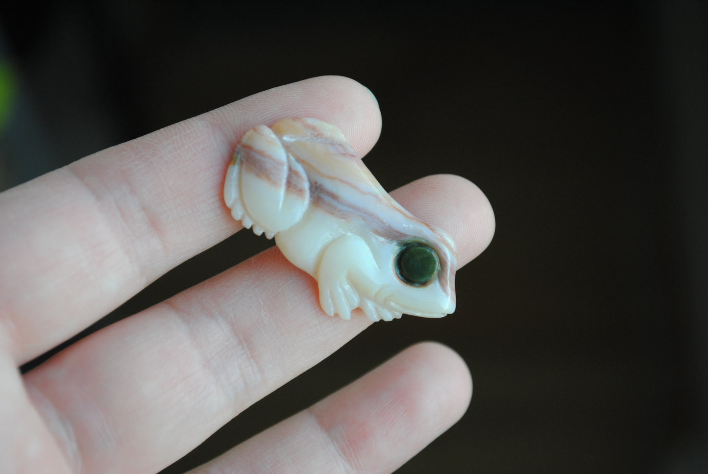 Small stone carving of a frog held in a hand against a dark background
