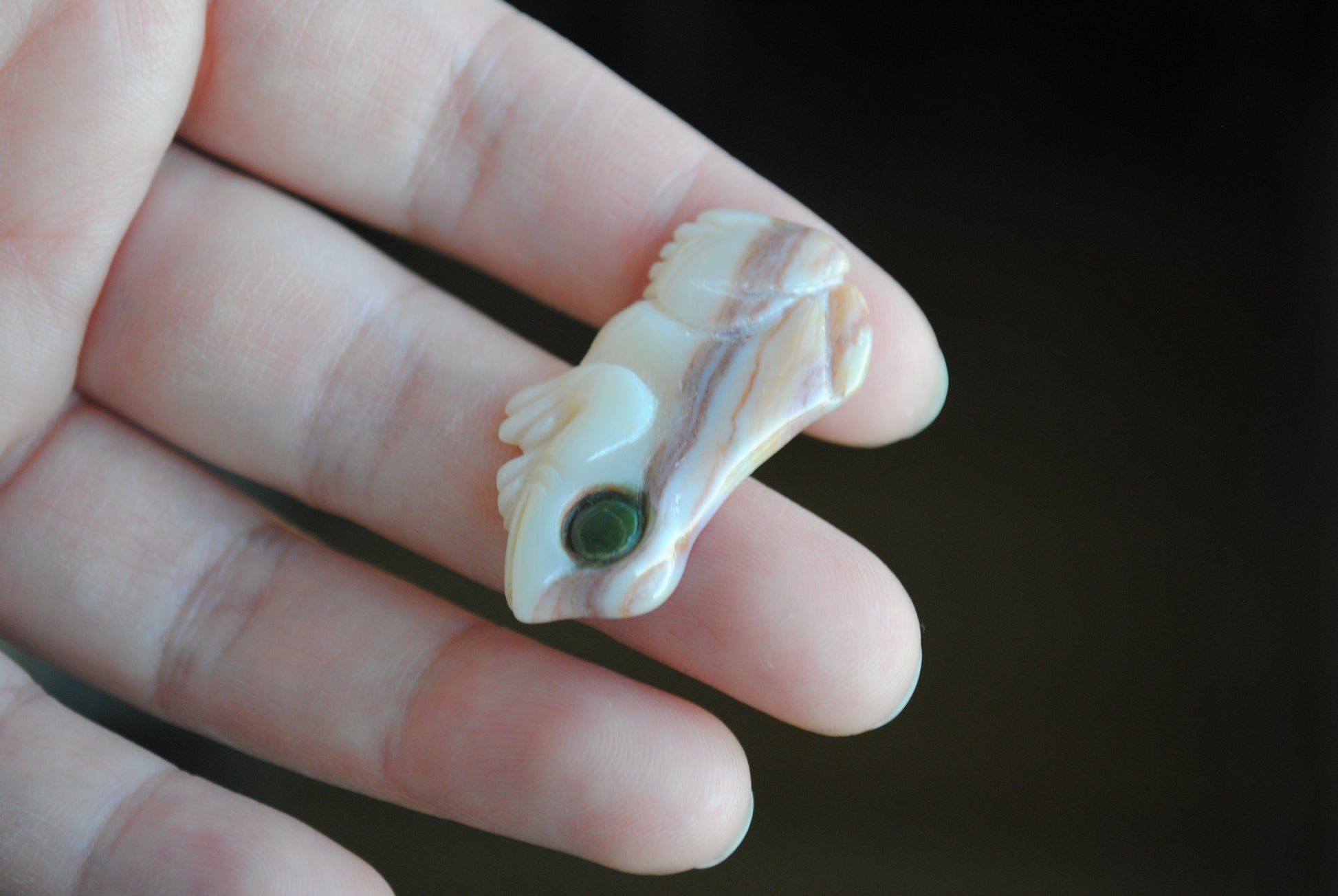 Small stone carving of a frog held in a hand against a dark background