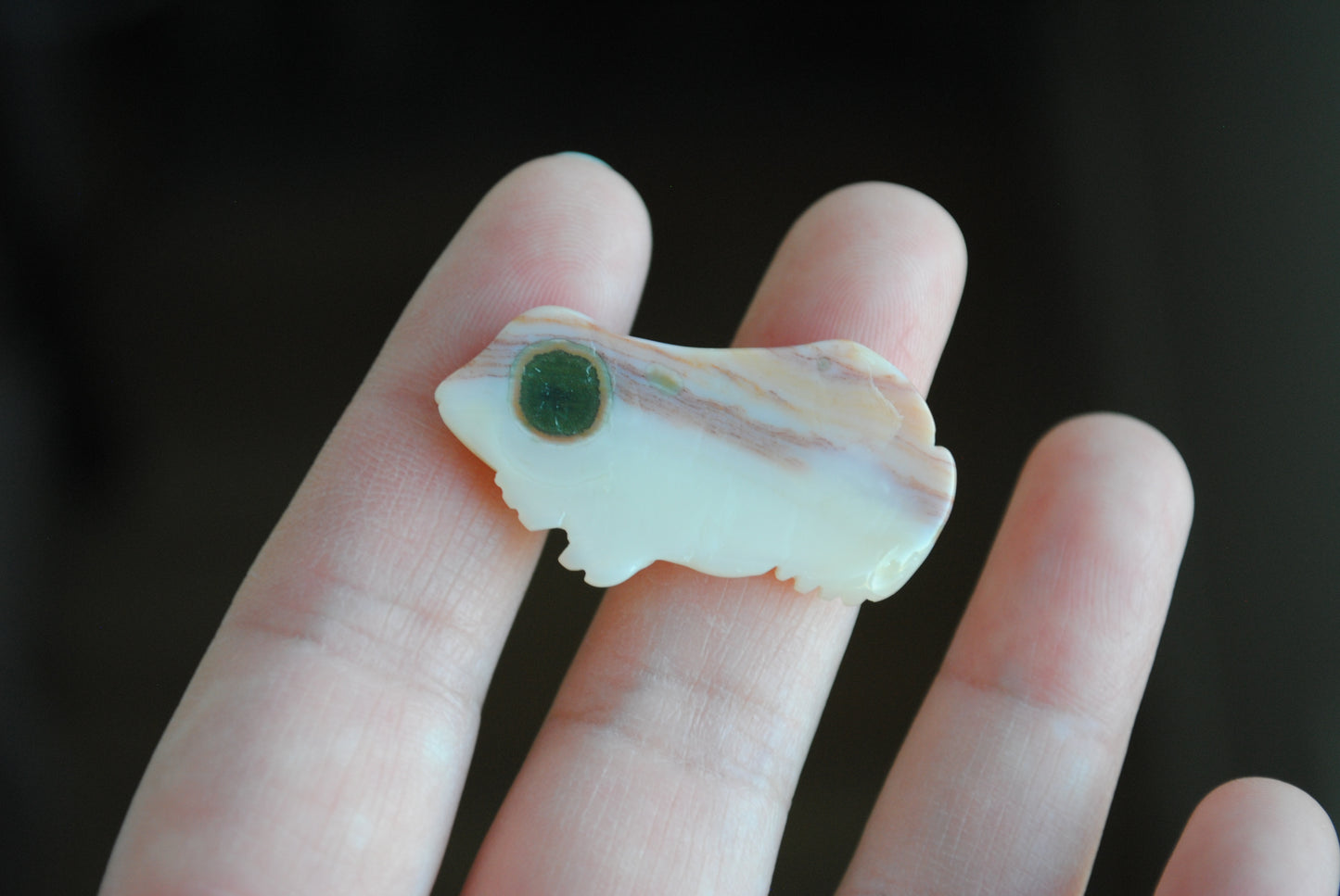Small stone carving of a frog held in a hand against a dark background