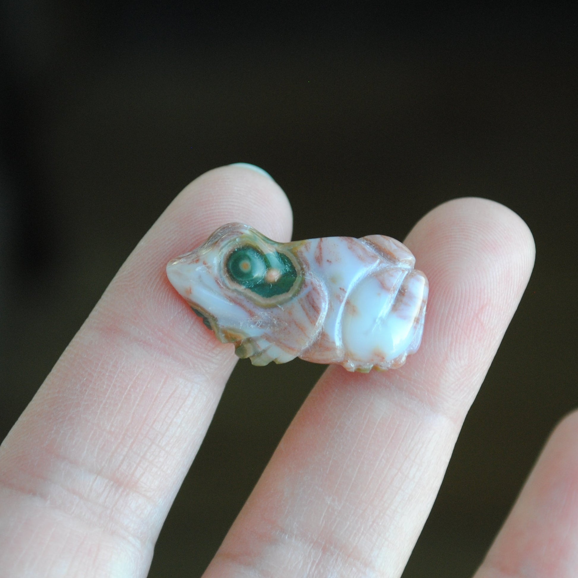 Small stone carving of a frog held in a hand against a dark background