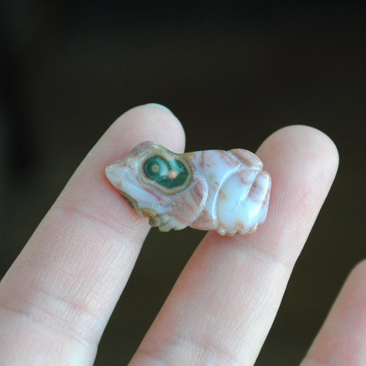 Small stone carving of a frog held in a hand against a dark background