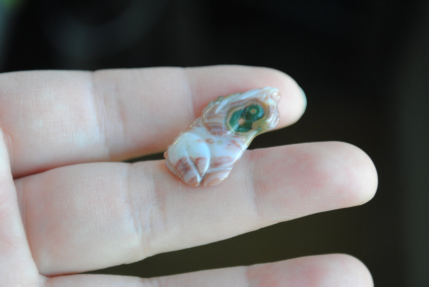 Small stone carving of a frog held in a hand against a dark background