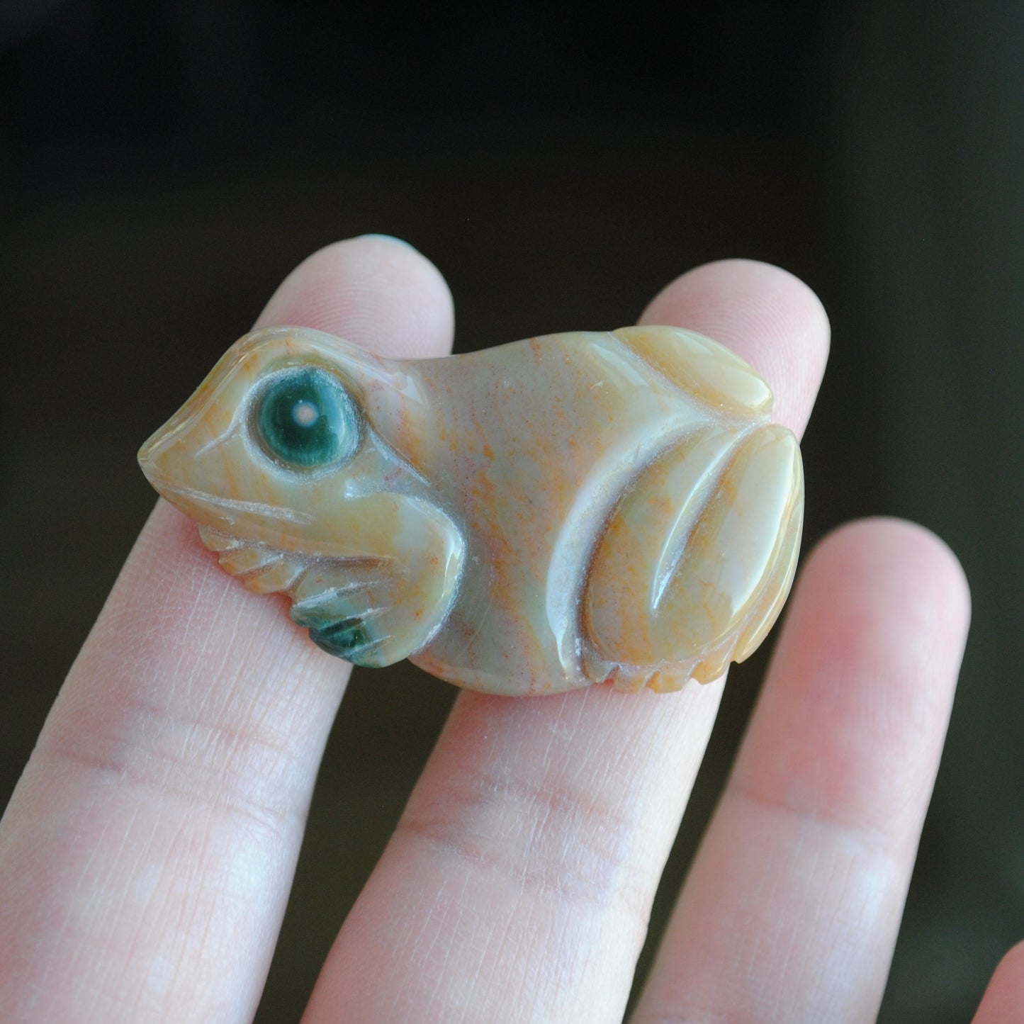 Small stone carving of a frog held in a hand against a dark background