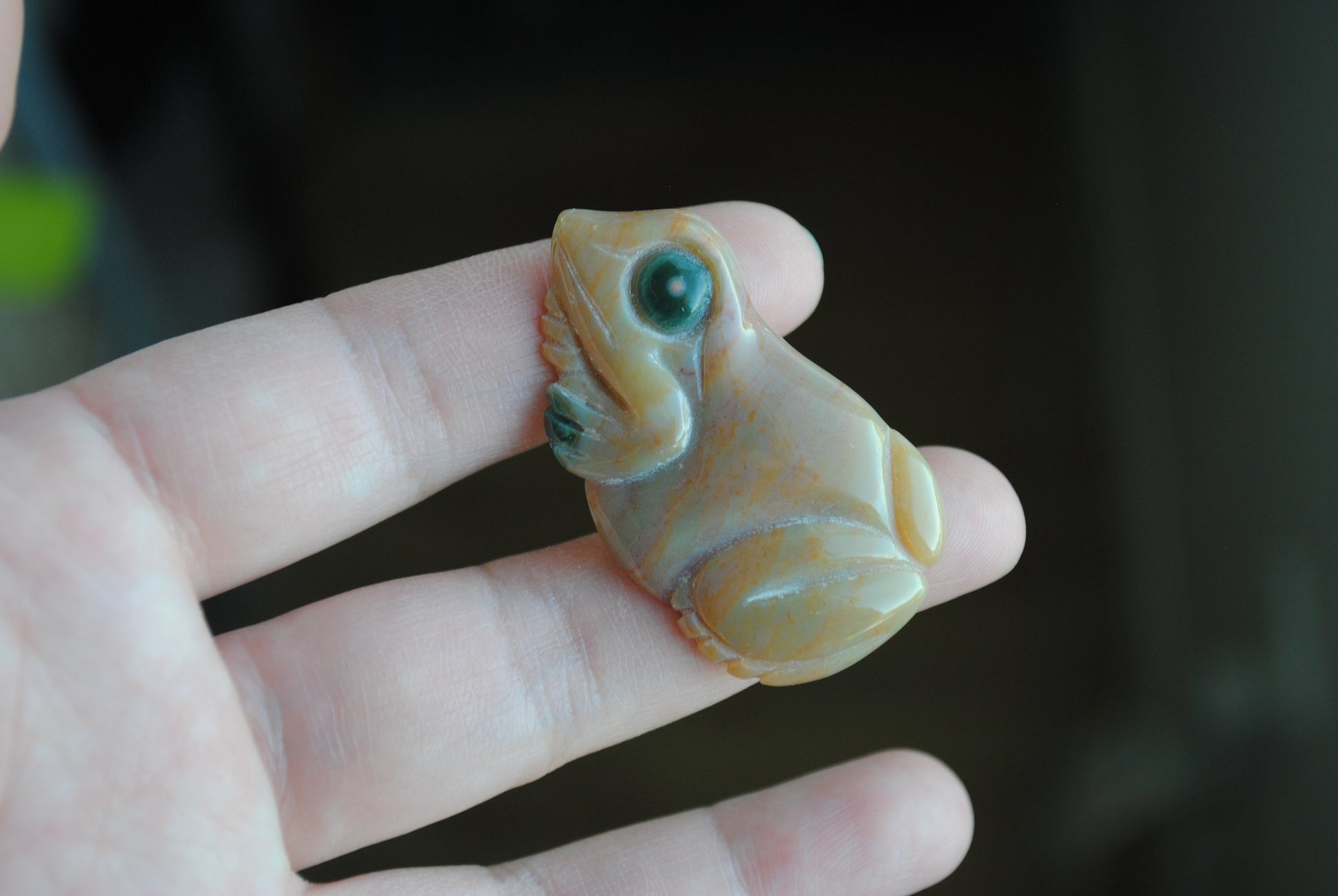 Small stone carving of a frog held in a hand against a dark background