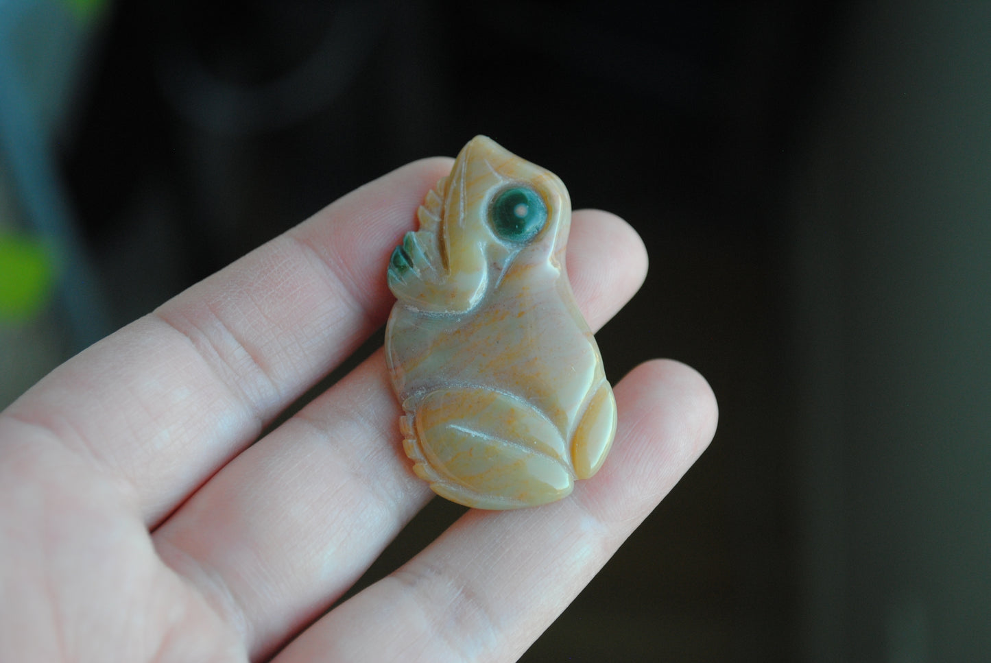 Small stone carving of a frog held in a hand against a dark background