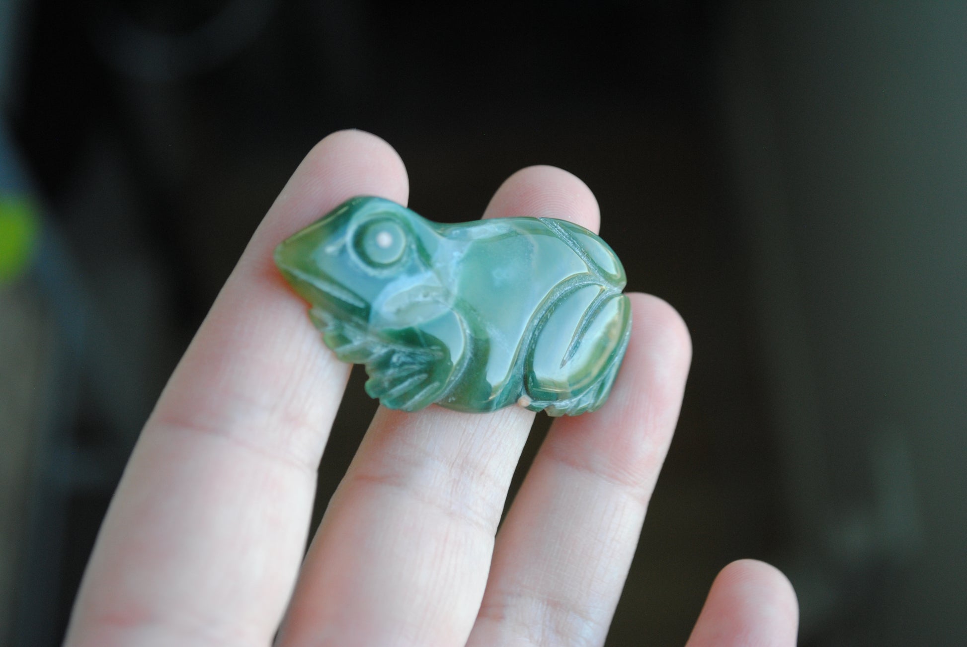 Hand holding a green stone carving of a frog against a blurred background