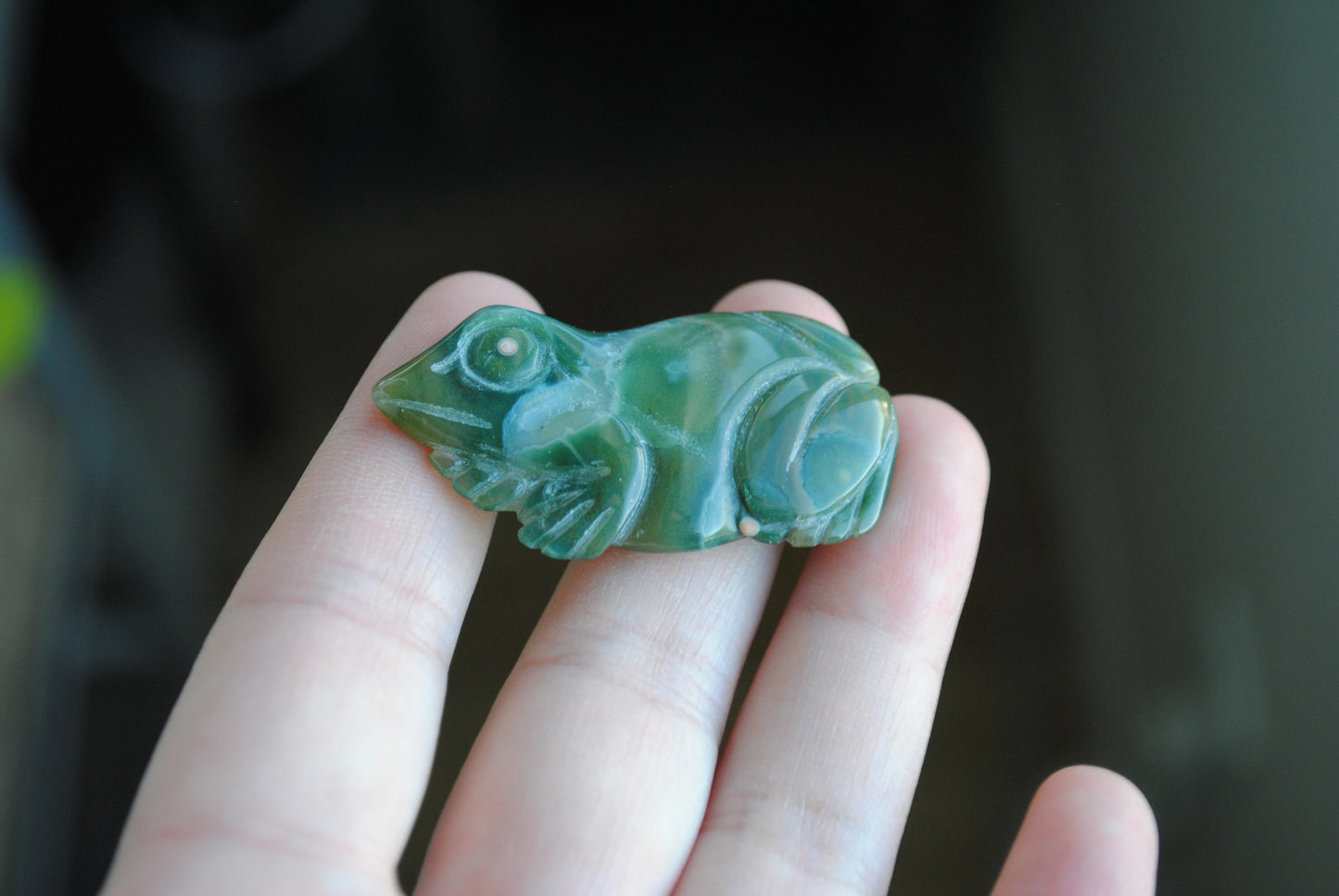 Hand holding a green stone carving of a frog against a blurred background