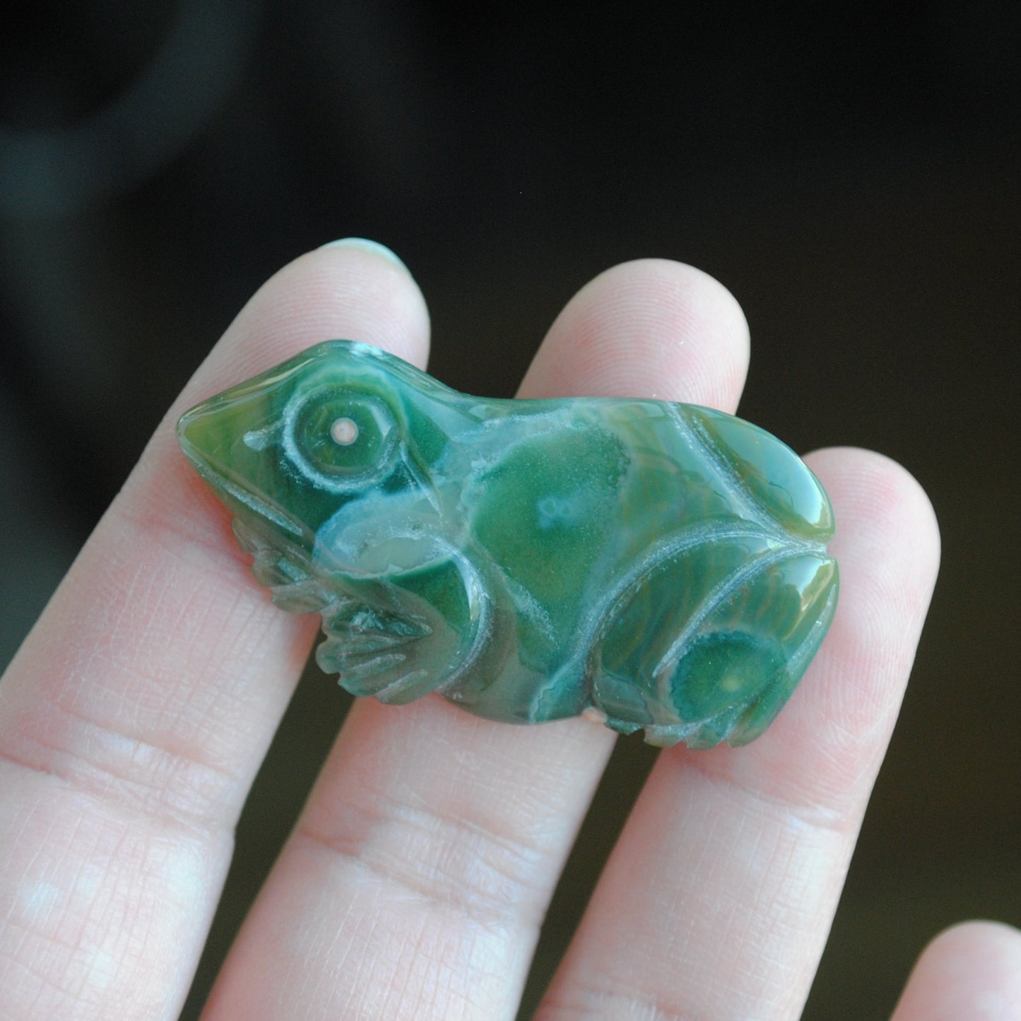 Hand holding a green stone carving of a frog against a blurred background