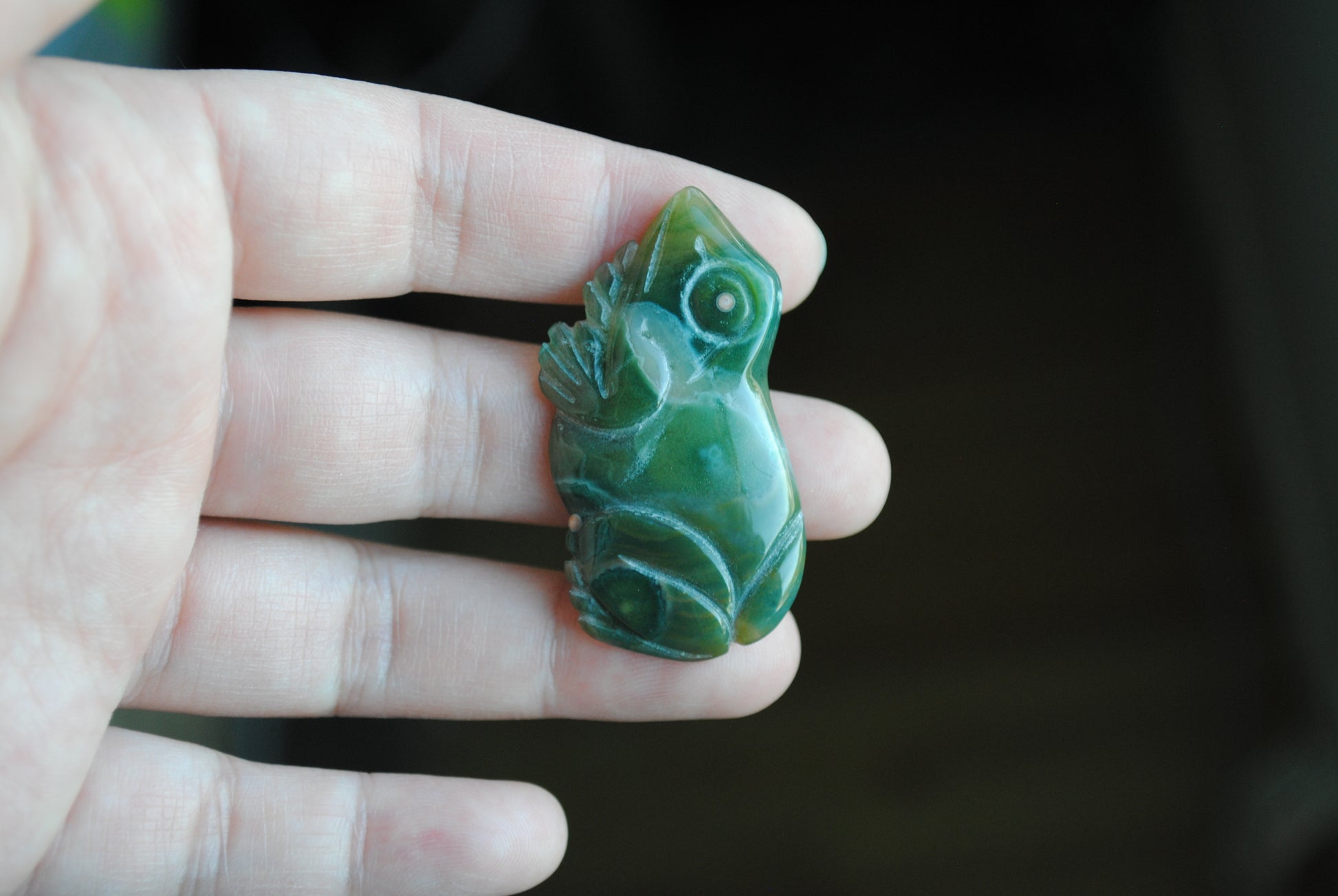 Hand holding a green stone carving of a frog against a blurred background