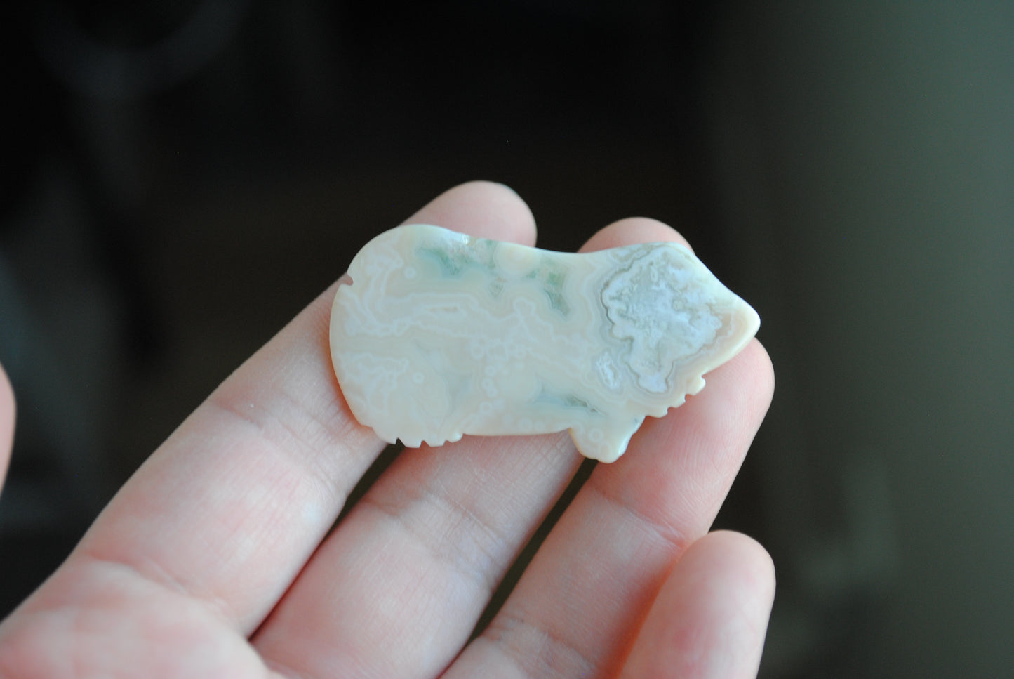 Carved stone frog held in a hand against a dark background