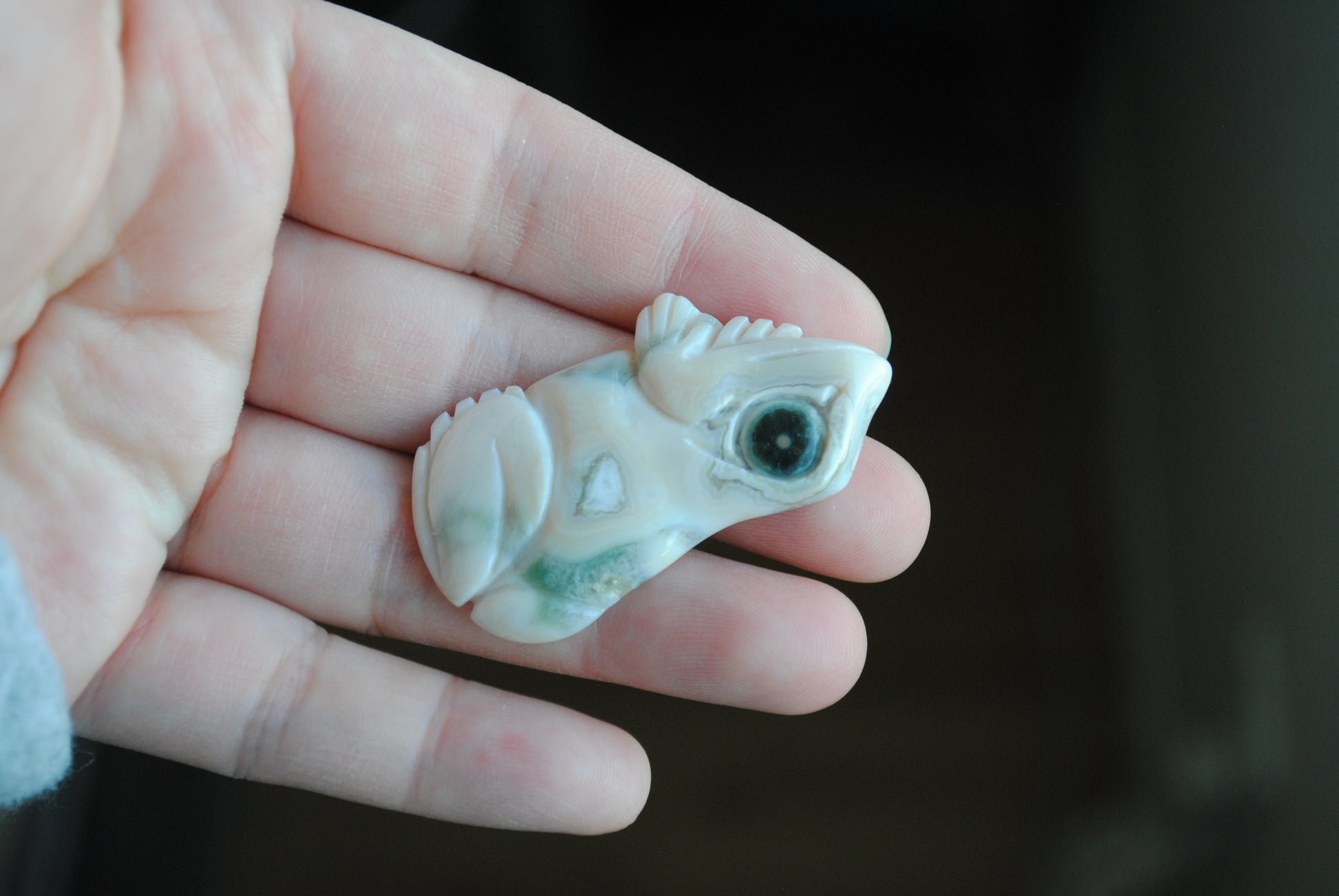Carved stone frog held in a hand against a dark background