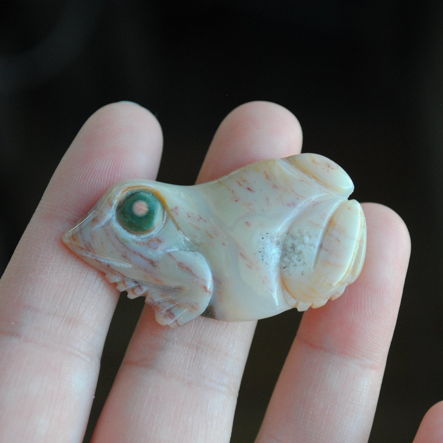 Carved stone frog held in a hand against a dark background