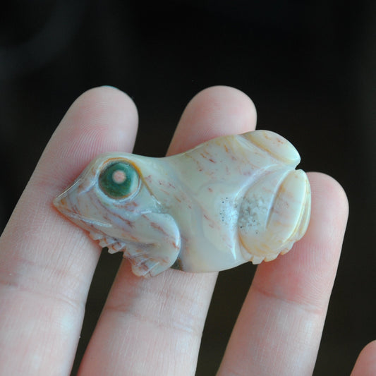Carved stone frog held in a hand against a dark background