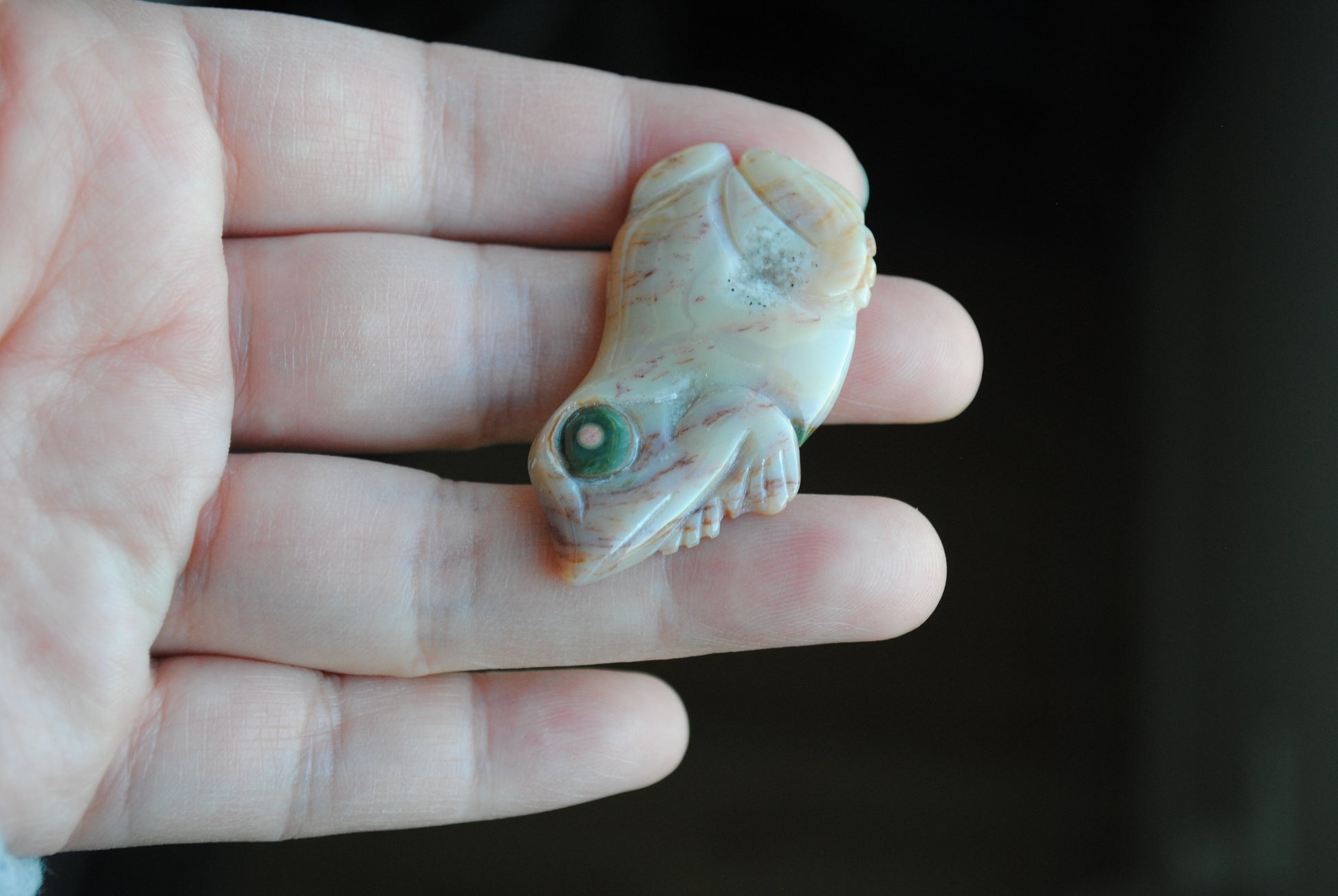 Carved stone frog held in a hand against a dark background
