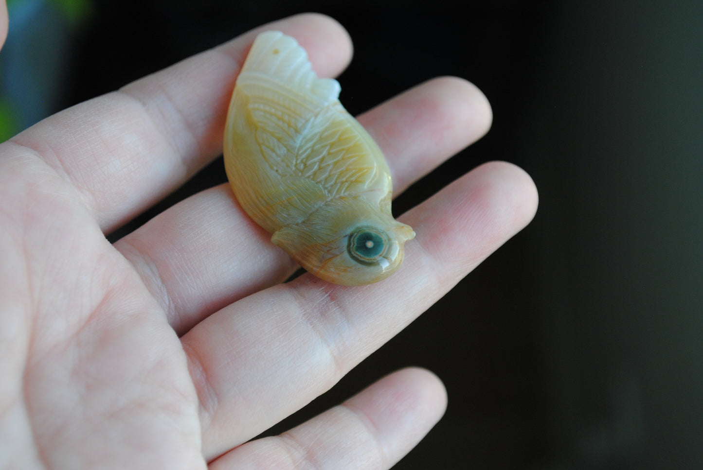 Ocean Jasper carved bird held in a hand against a blurred background