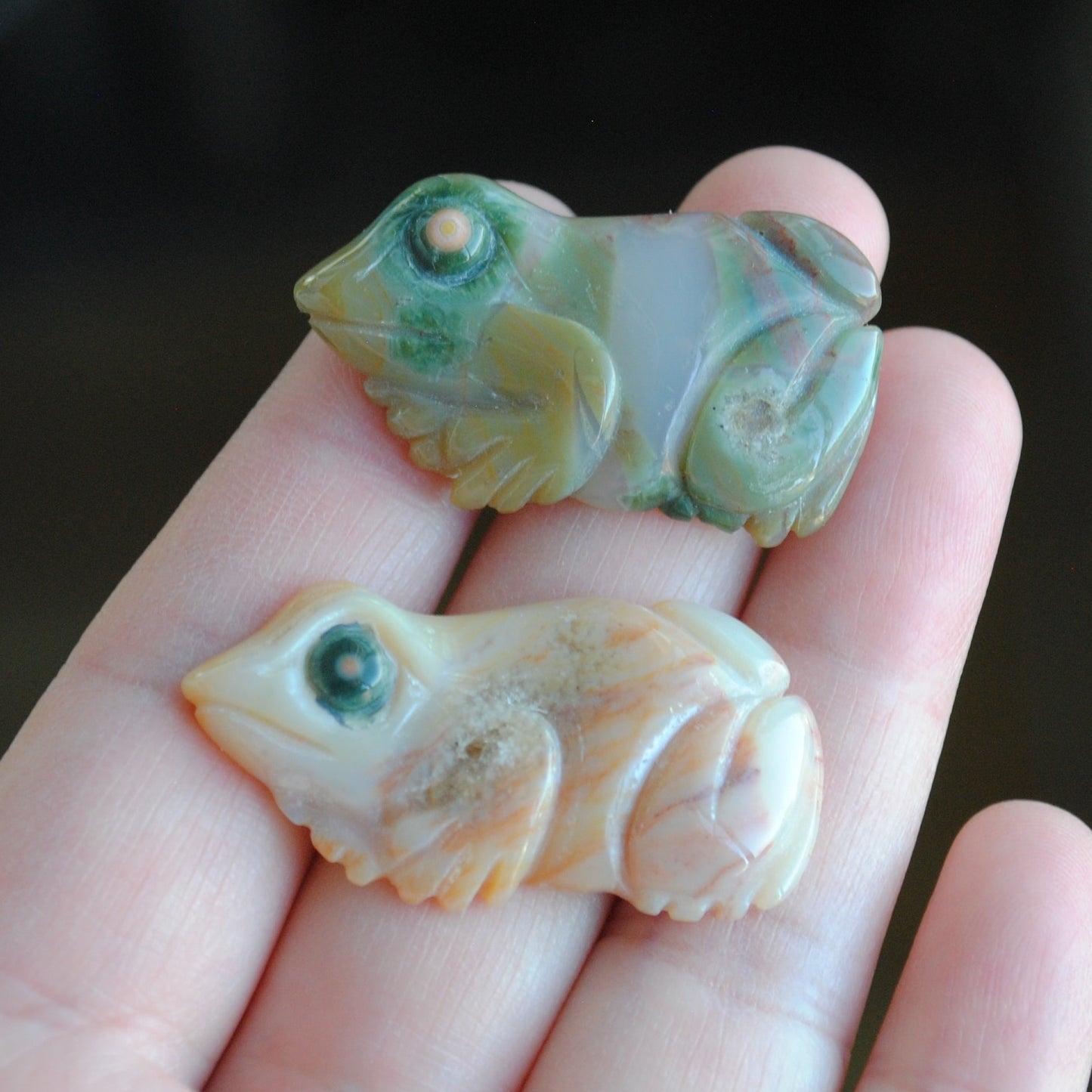 Two small stone frog carvings held in a hand against a blurred background