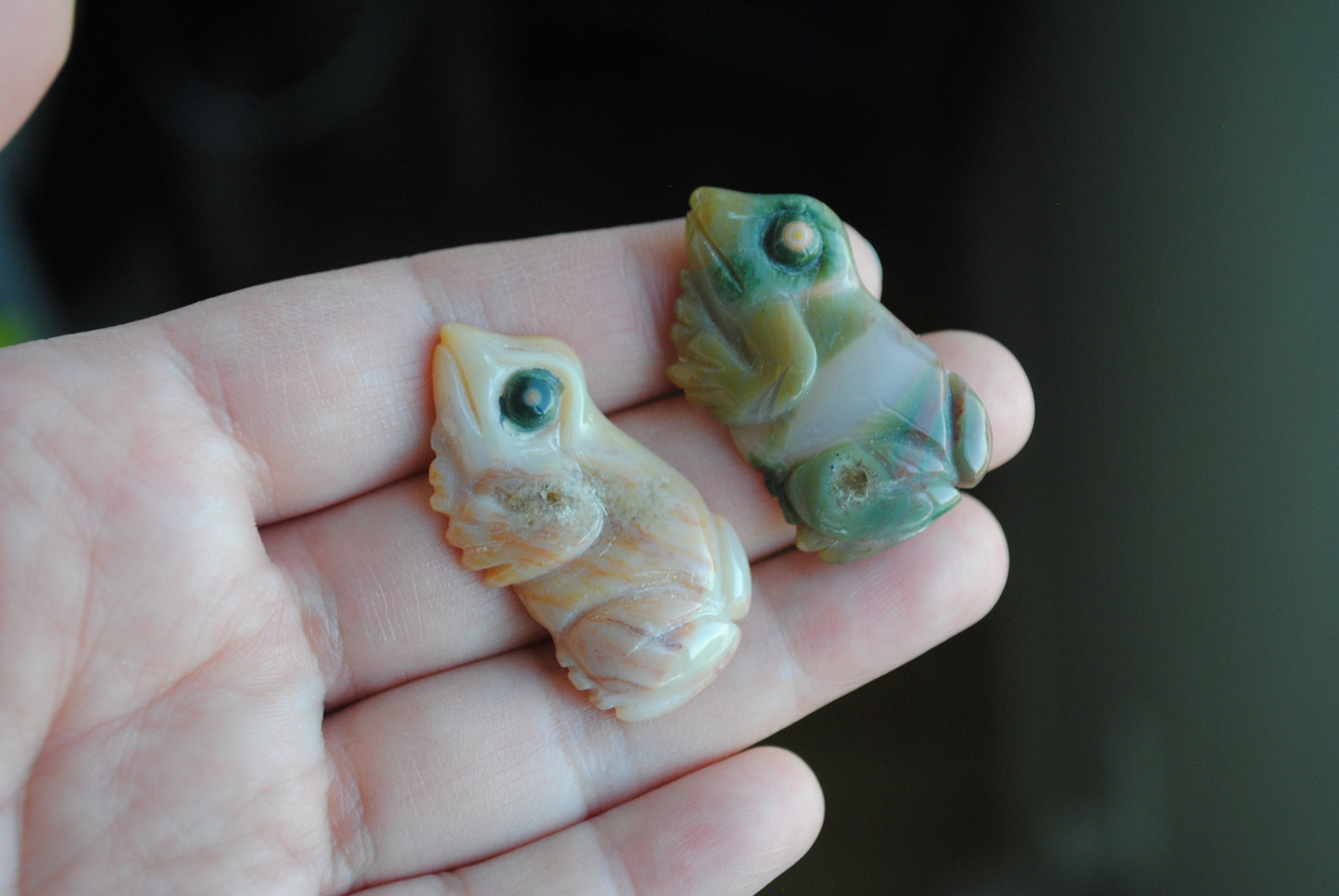 Two small stone frog carvings held in a hand against a blurred background