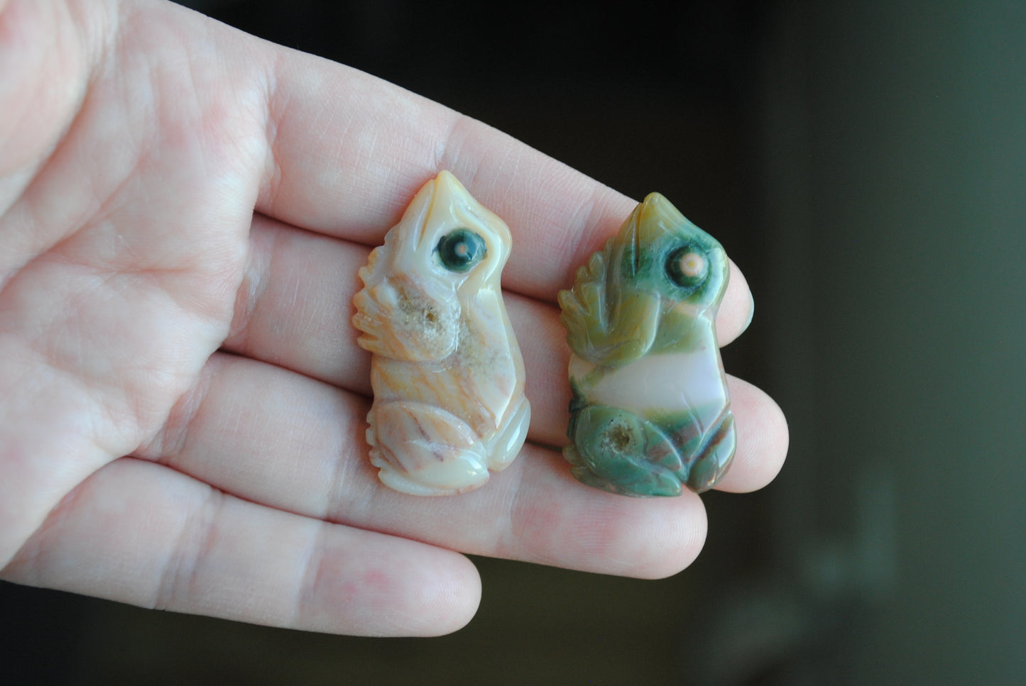 Two small stone frog carvings held in a hand against a blurred background