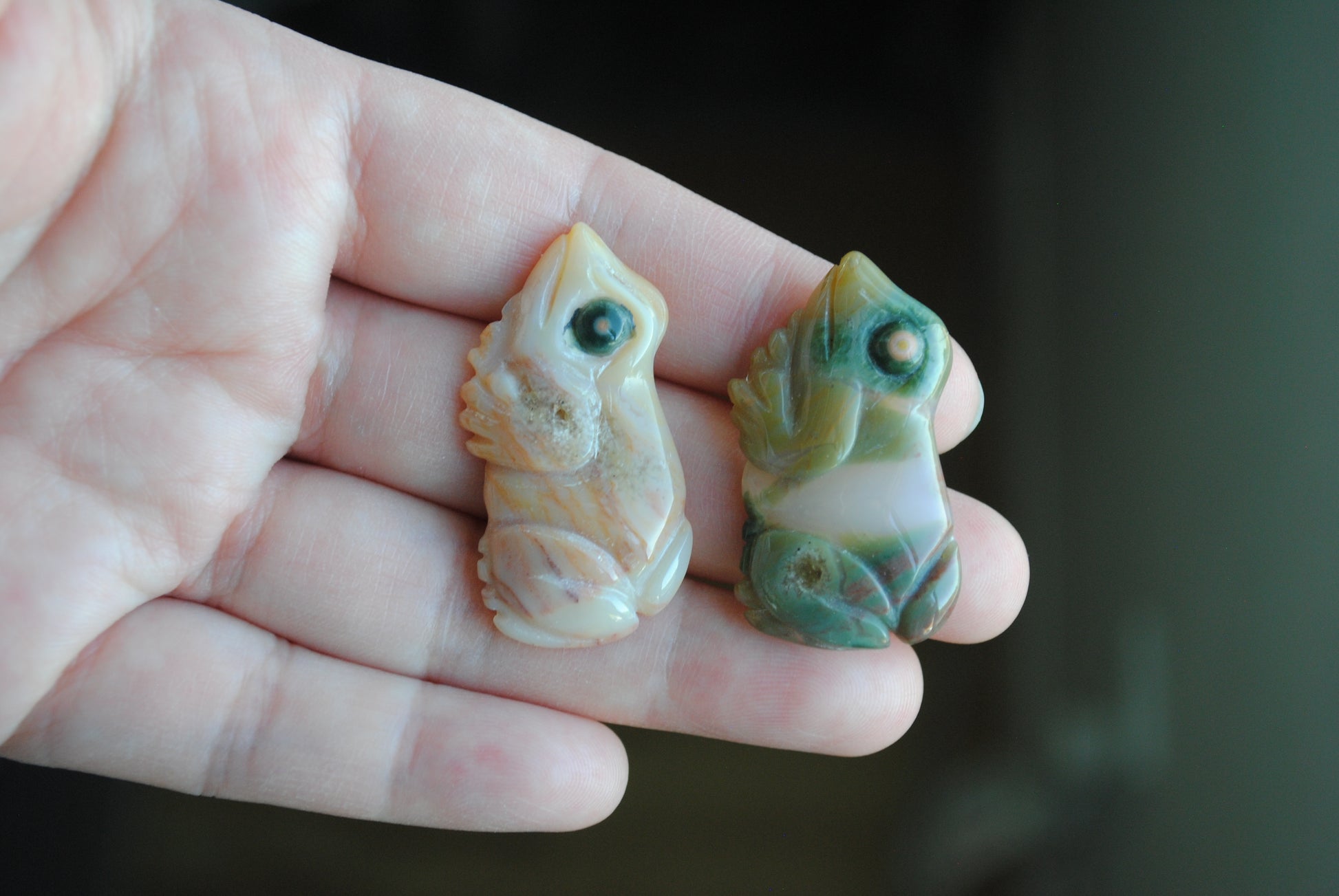 Two small stone frog carvings held in a hand against a blurred background