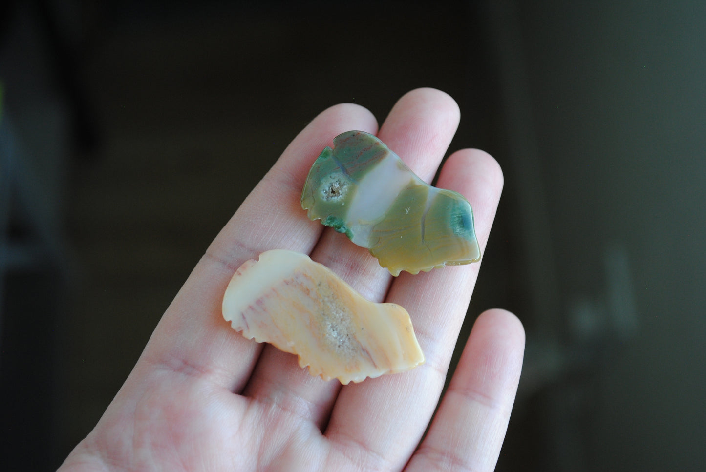 Two small stone frog carvings held in a hand against a blurred background