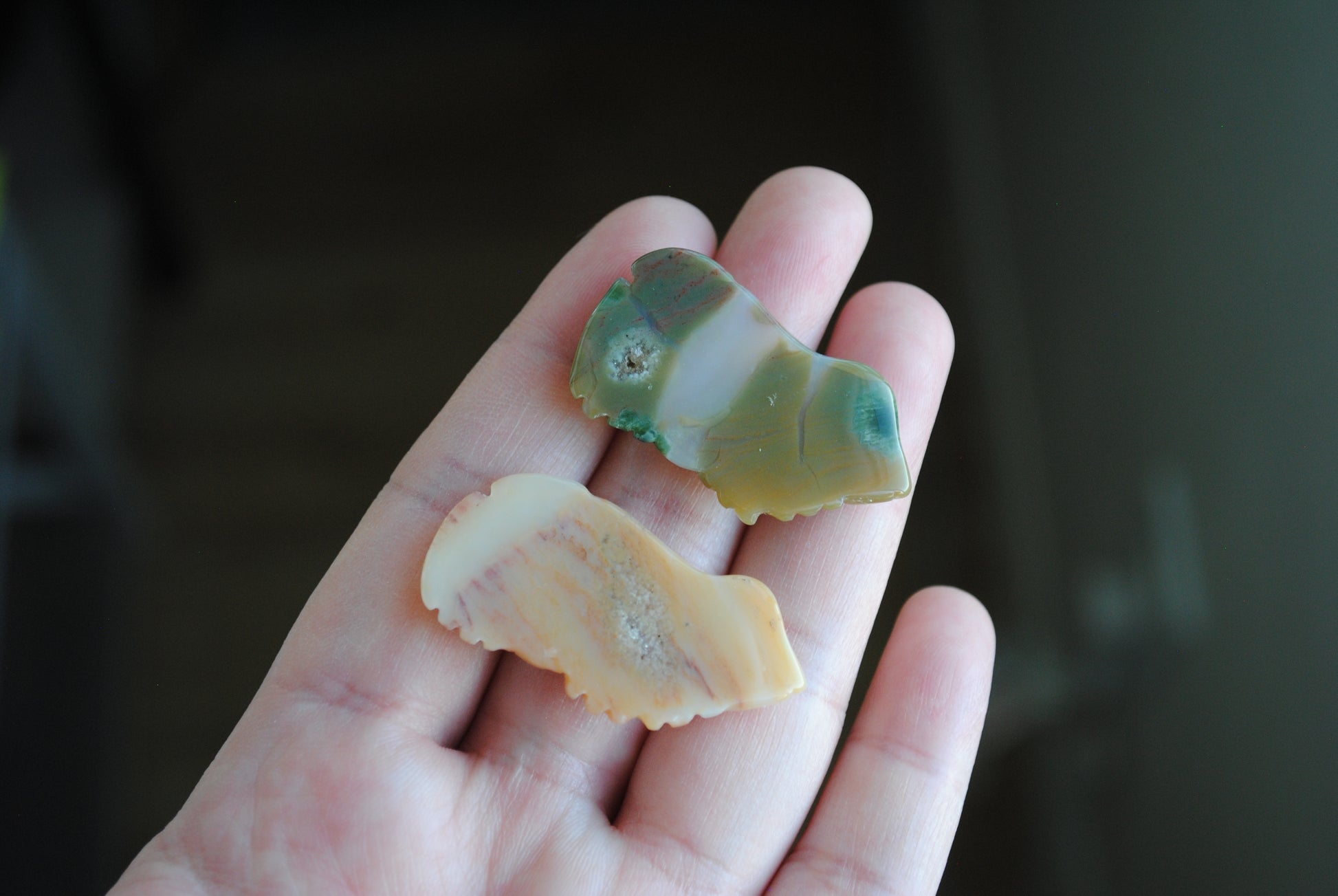 Two small stone frog carvings held in a hand against a blurred background