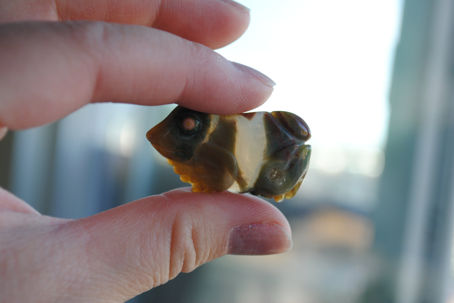 Small stone frog carving held in a hand against a blurred background