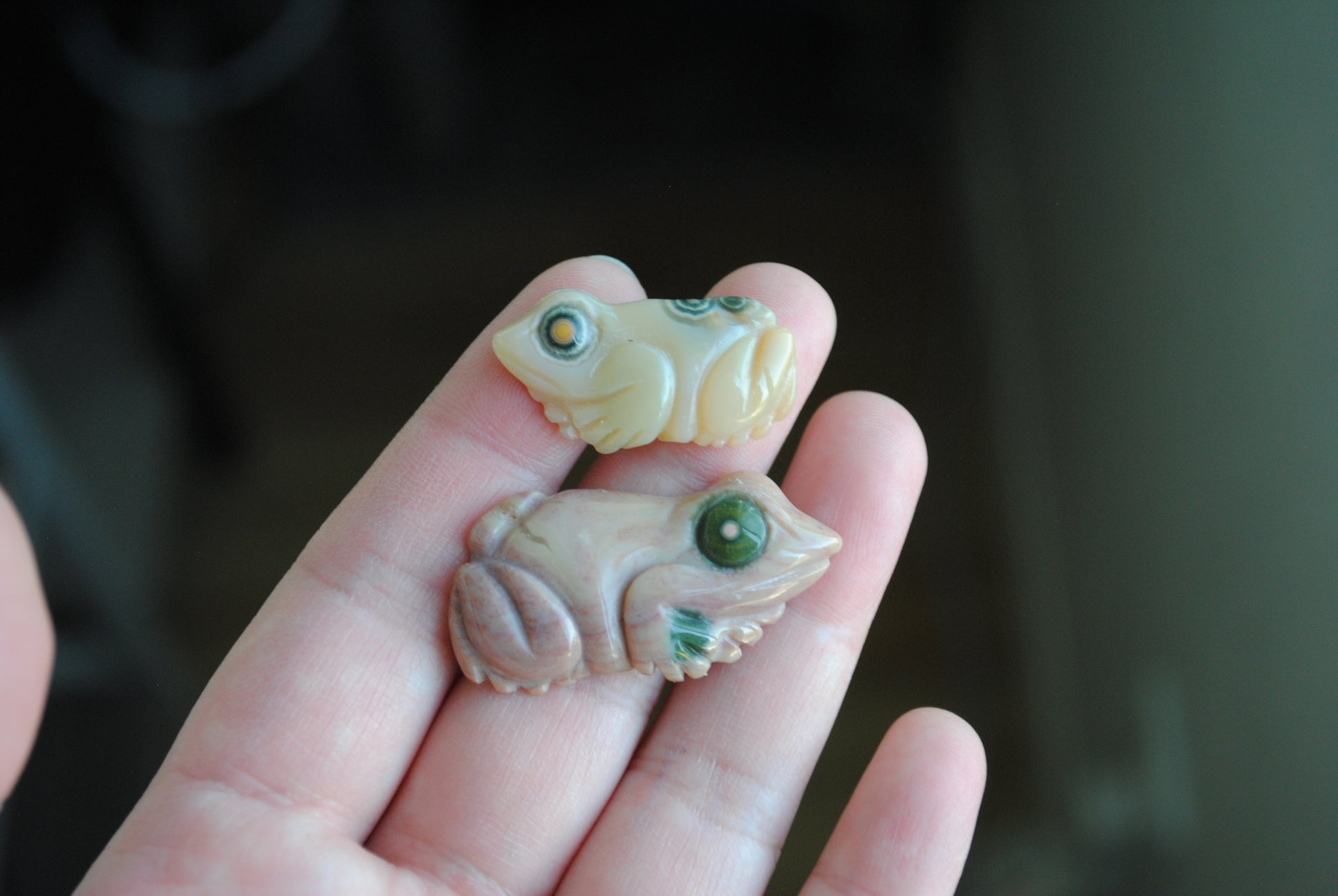 Two small stone frog carvings held in a hand against a blurred background