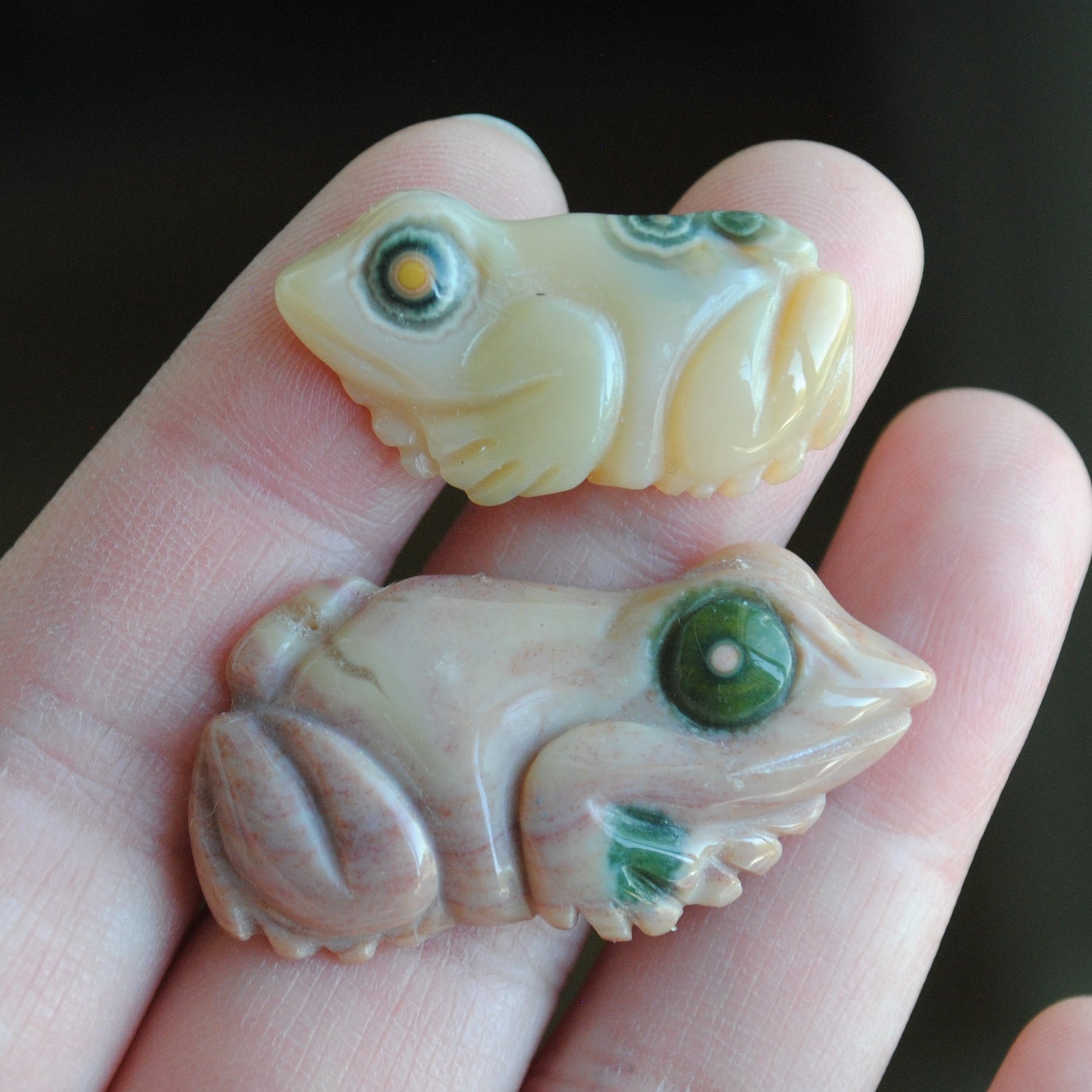 Two small stone frog carvings held in a hand against a blurred background