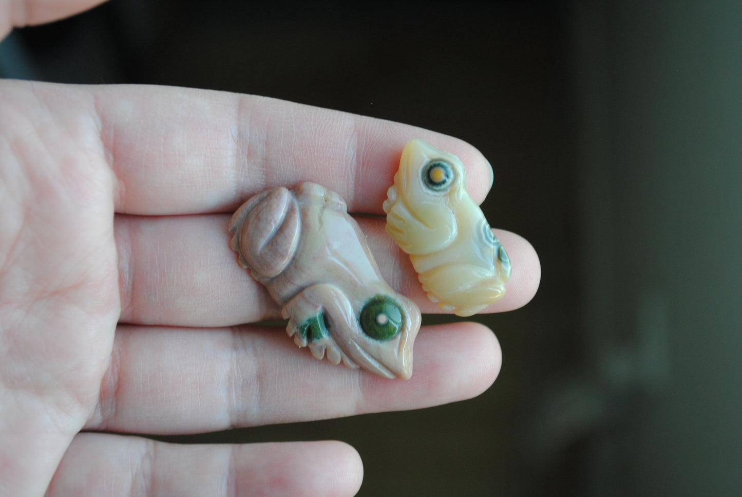 Two small stone frog carvings held in a hand against a blurred background