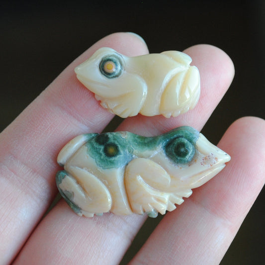 Two small stone frog carvings held in a hand against a blurred background