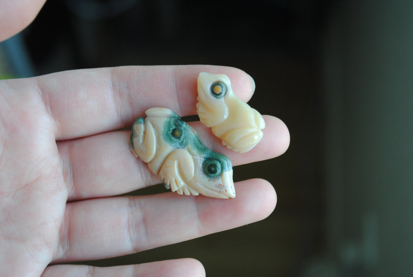 Two small stone frog carvings held in a hand against a blurred background