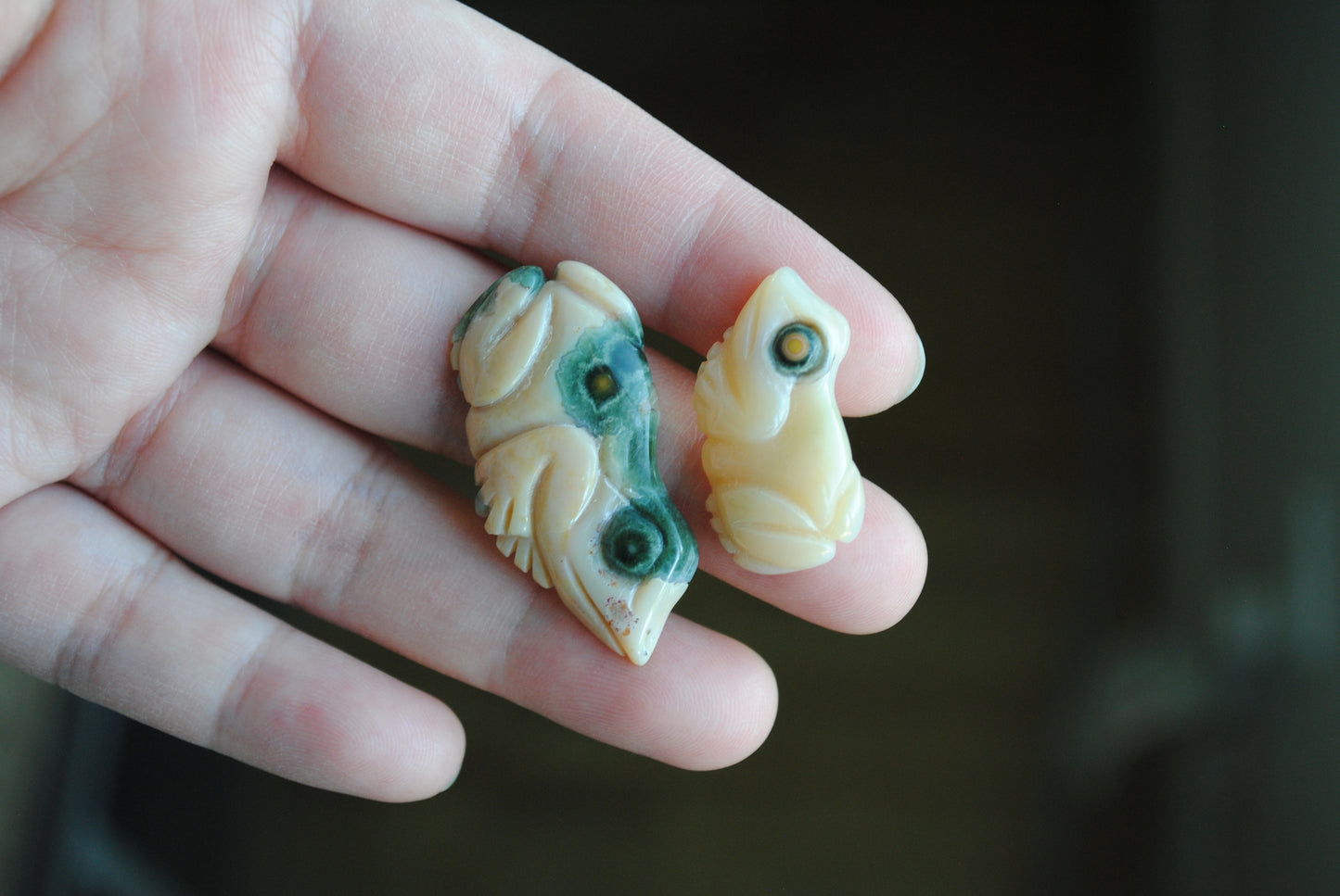 Two small stone frog carvings held in a hand against a blurred background