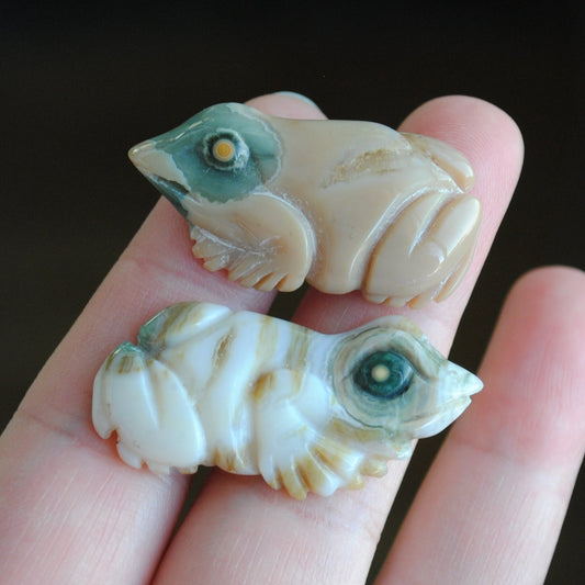 Two small stone frog carvings held in a hand against a blurred background