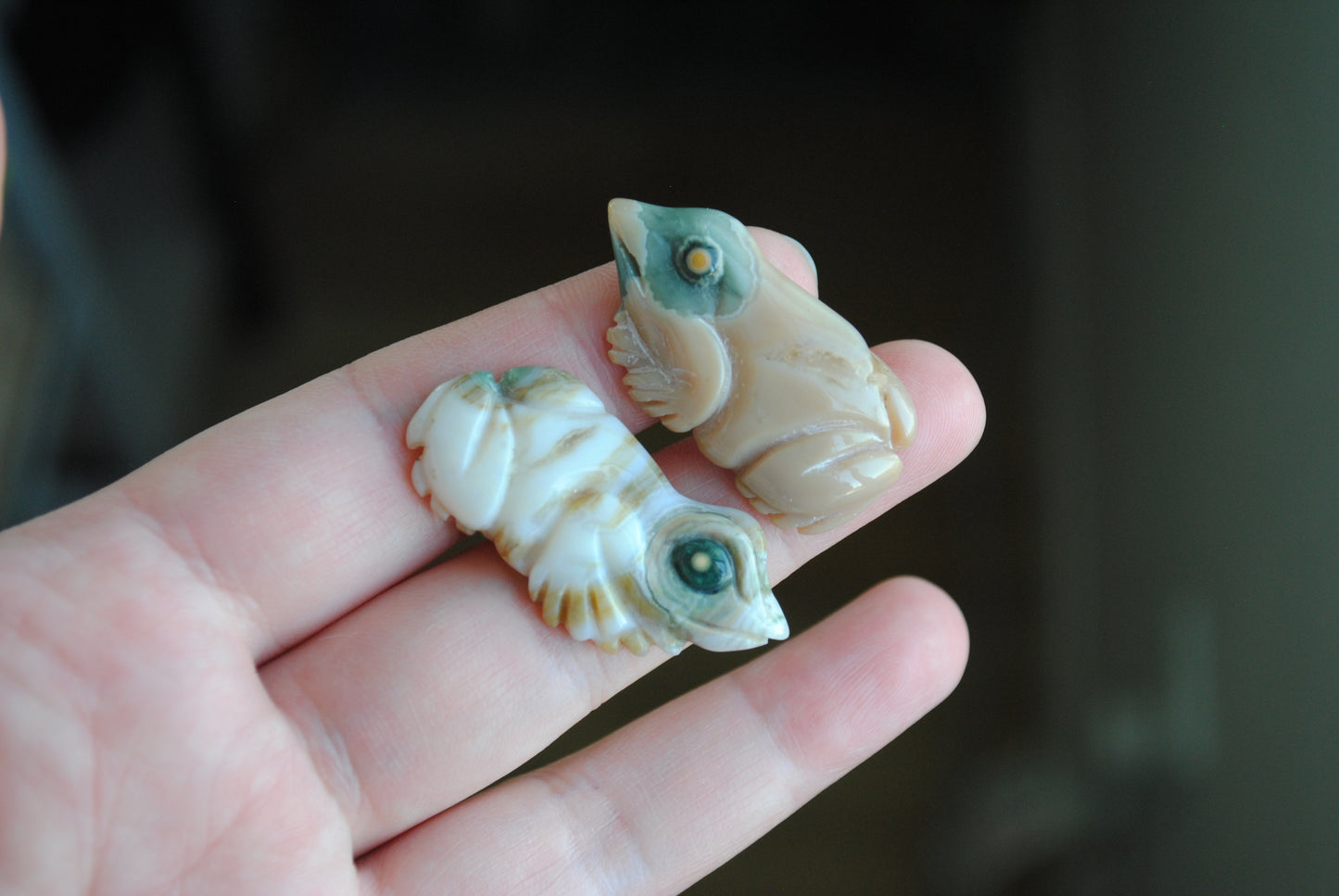 Two small stone frog carvings held in a hand against a blurred background