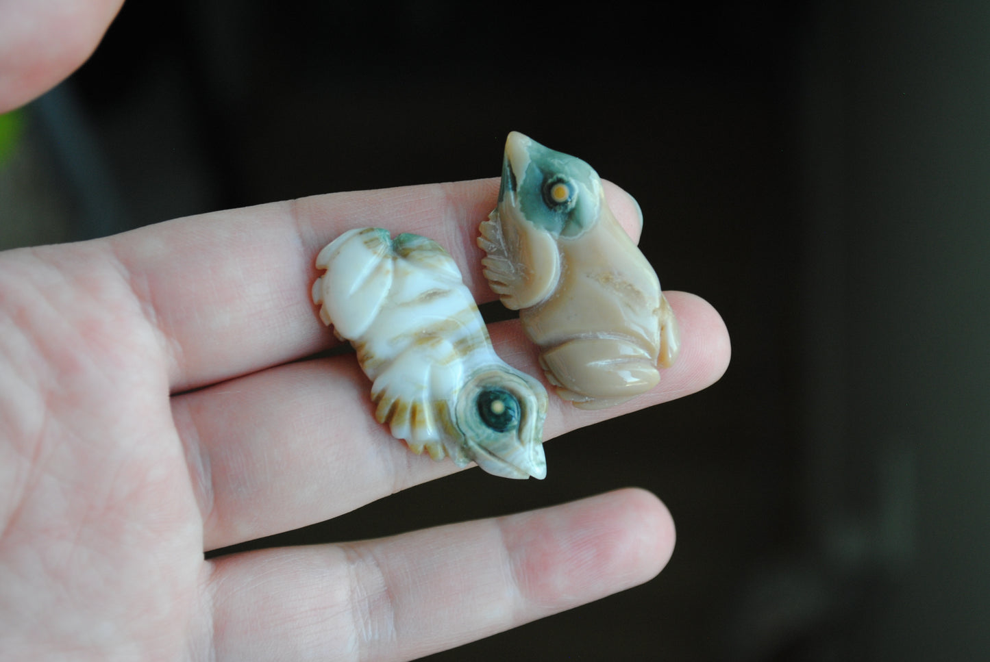 Two small stone frog carvings held in a hand against a blurred background