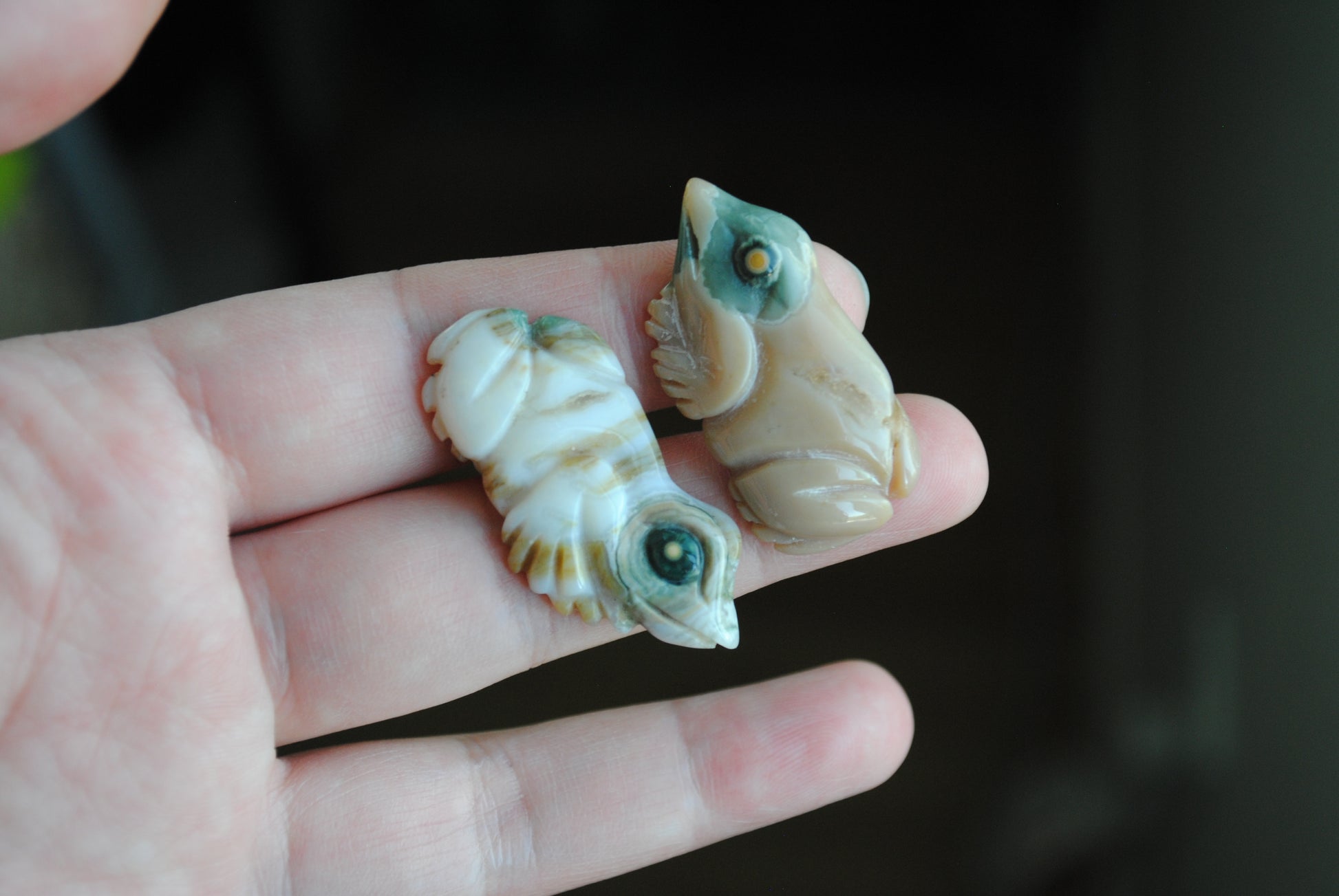 Two small stone frog carvings held in a hand against a blurred background
