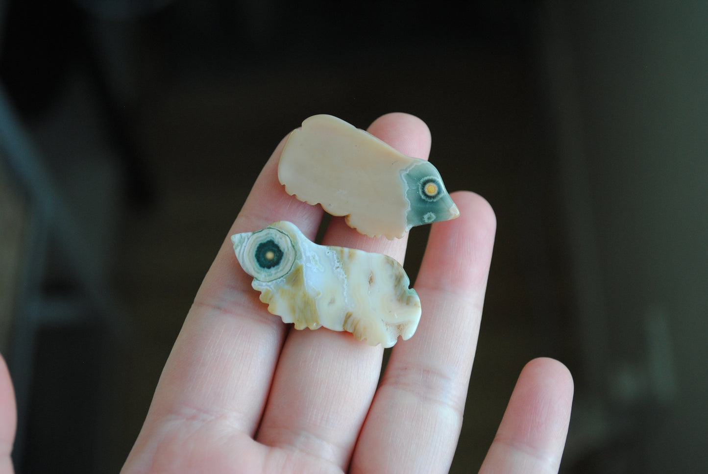 Two small stone frog carvings held in a hand against a blurred background