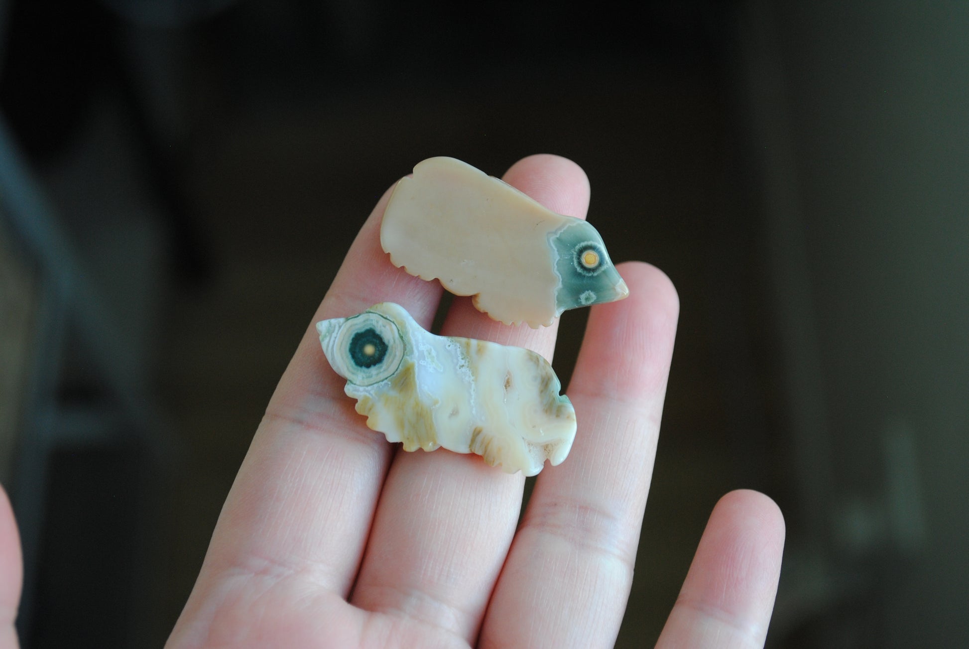 Two small stone frog carvings held in a hand against a blurred background
