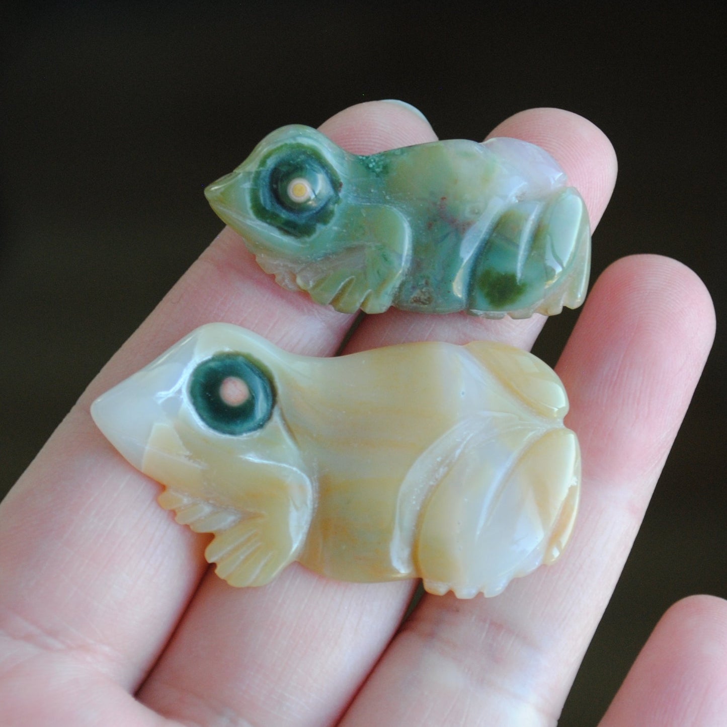 Two small stone frog carvings held in a hand against a blurred background