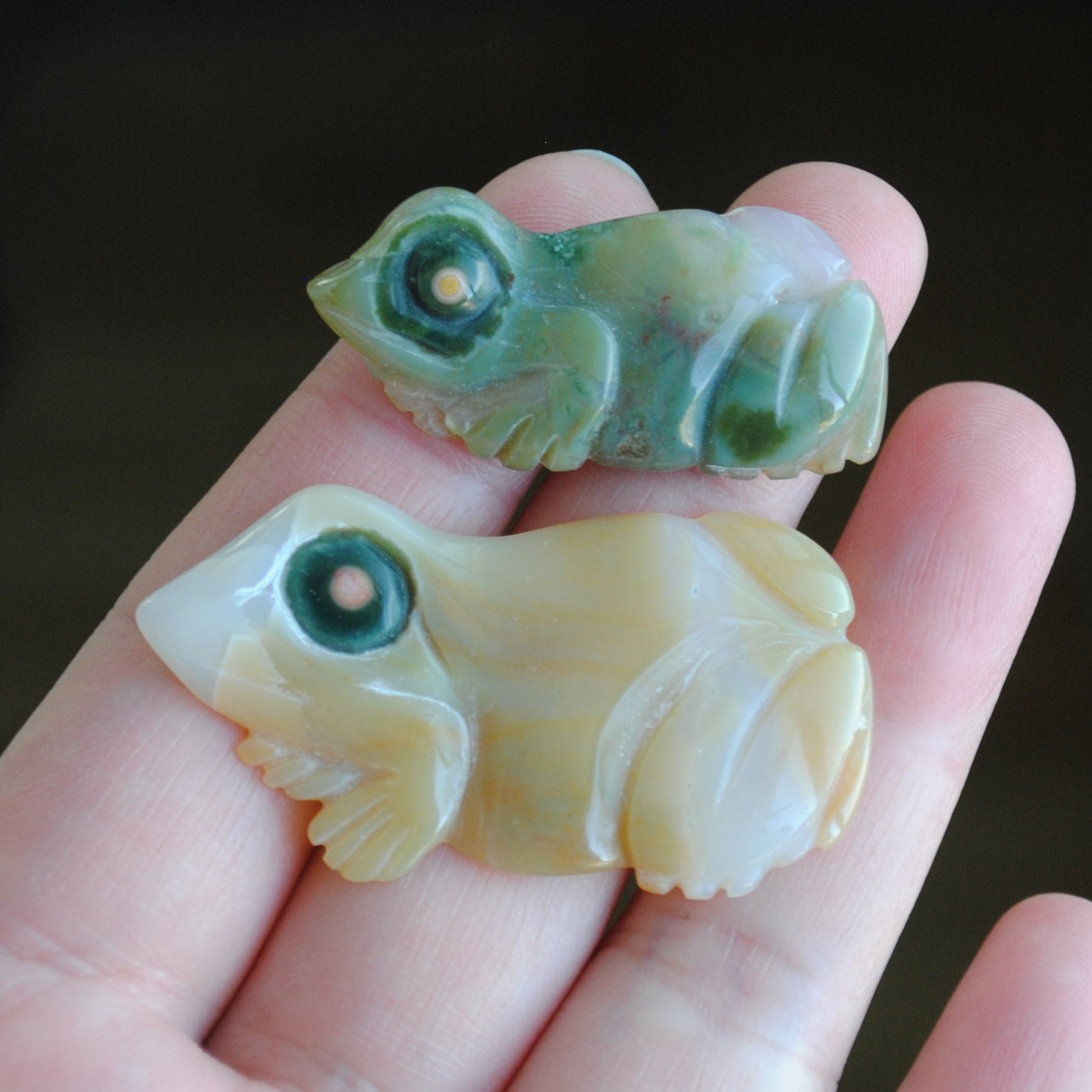 Two small stone frog carvings held in a hand against a blurred background