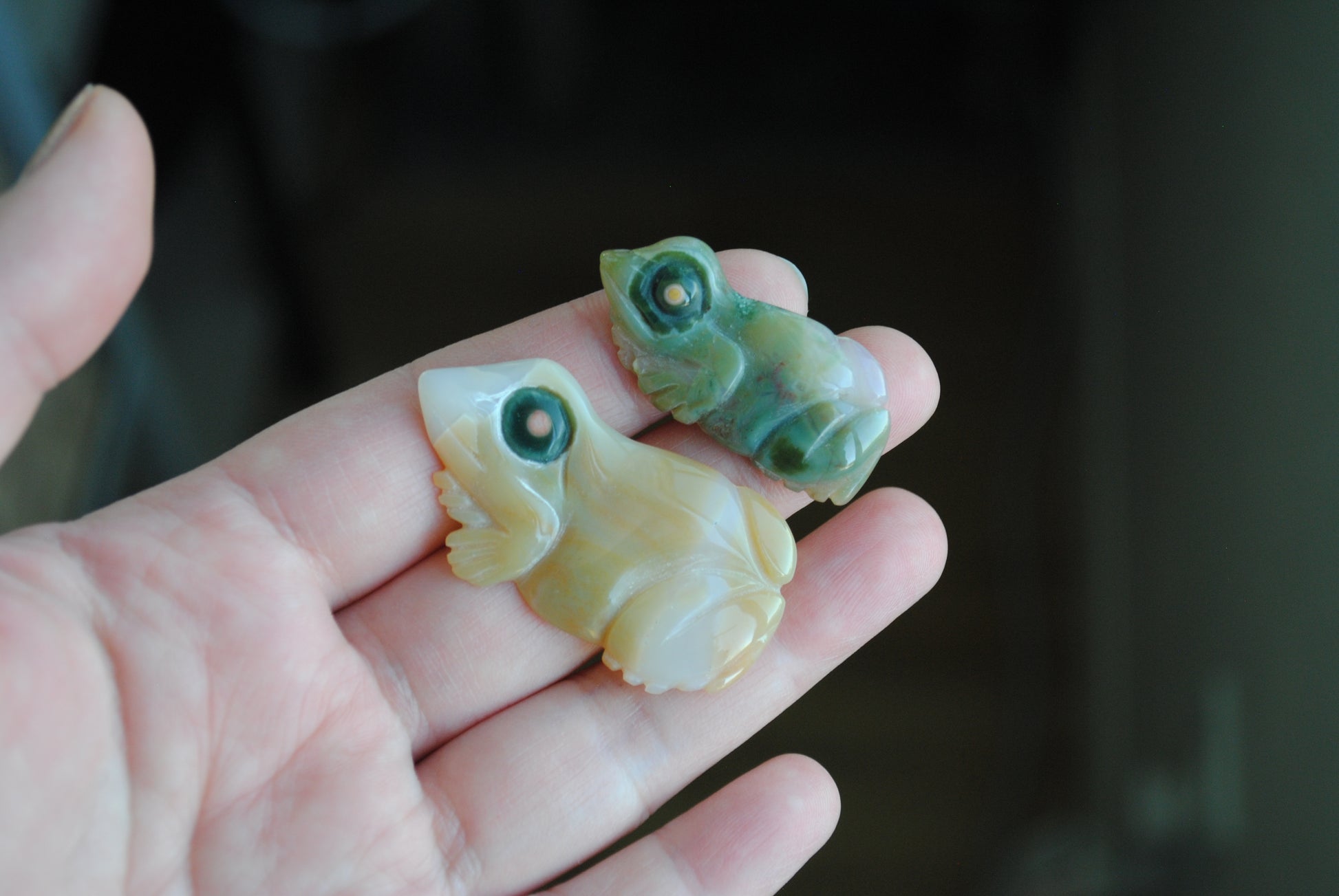 Two small stone frog carvings held in a hand against a blurred background